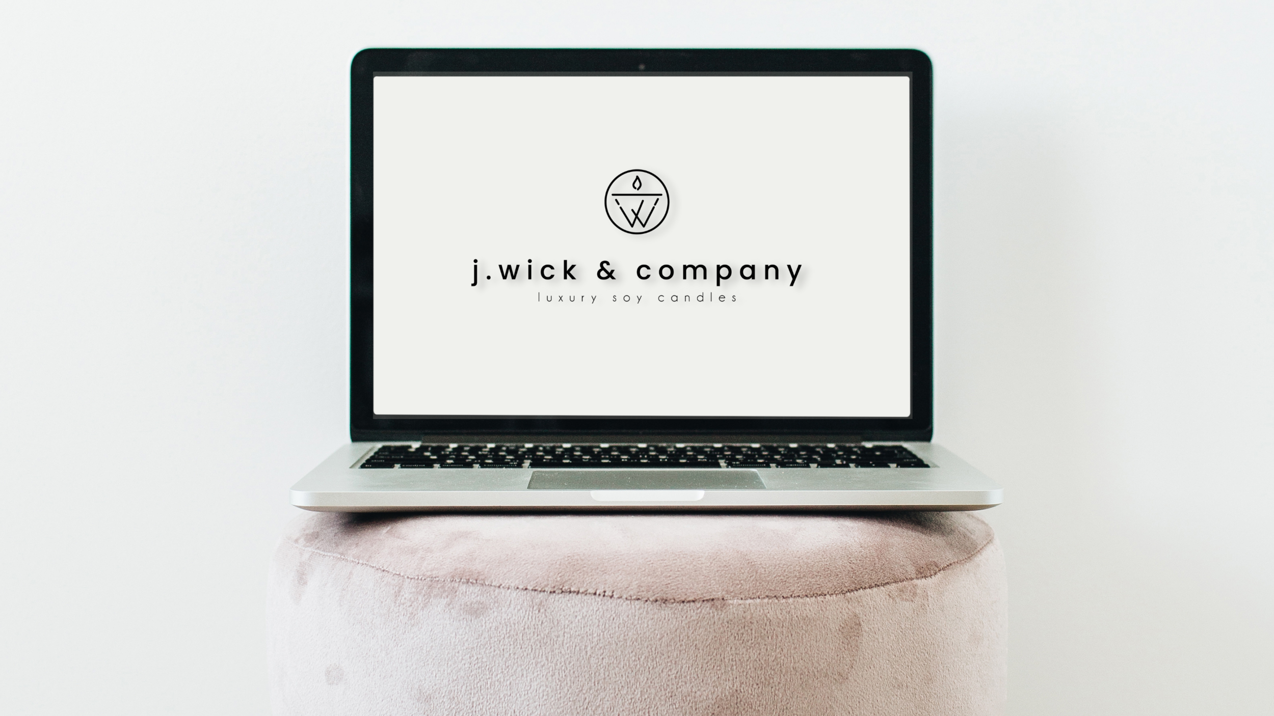 Laptop displaying the logo and name of j.wick & company, luxury soy candles, on a soft pink pedestal against a white background. Logo designed by Brim and Bold Creative.