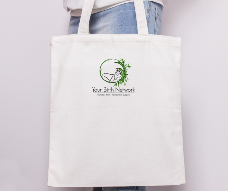 White tote bag with a logo of a sleeping baby curled in a circle with green foliage, and the text 'Your Birth Network' underneath, along with the words 'Prenatal - Birth - Postpartum Support.' Logo designed by Brim and Bold Creative.