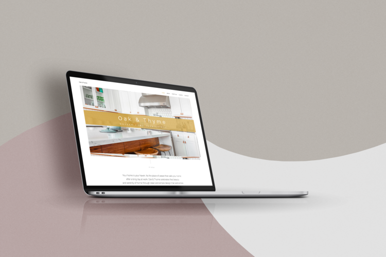 A silver laptop with a black screen displaying a website titled 'Oak & Thyme' showing a kitchen interior. The laptop is placed on a white surface against a modern. Website designed by Brim and Bold Creative.