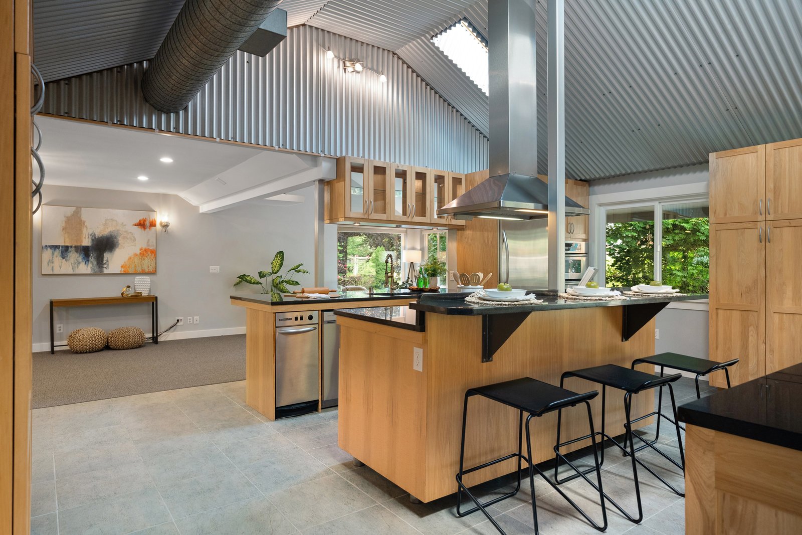 view of the kitchen with light wood cabinets and black granite countertops with a stand alone stove vent