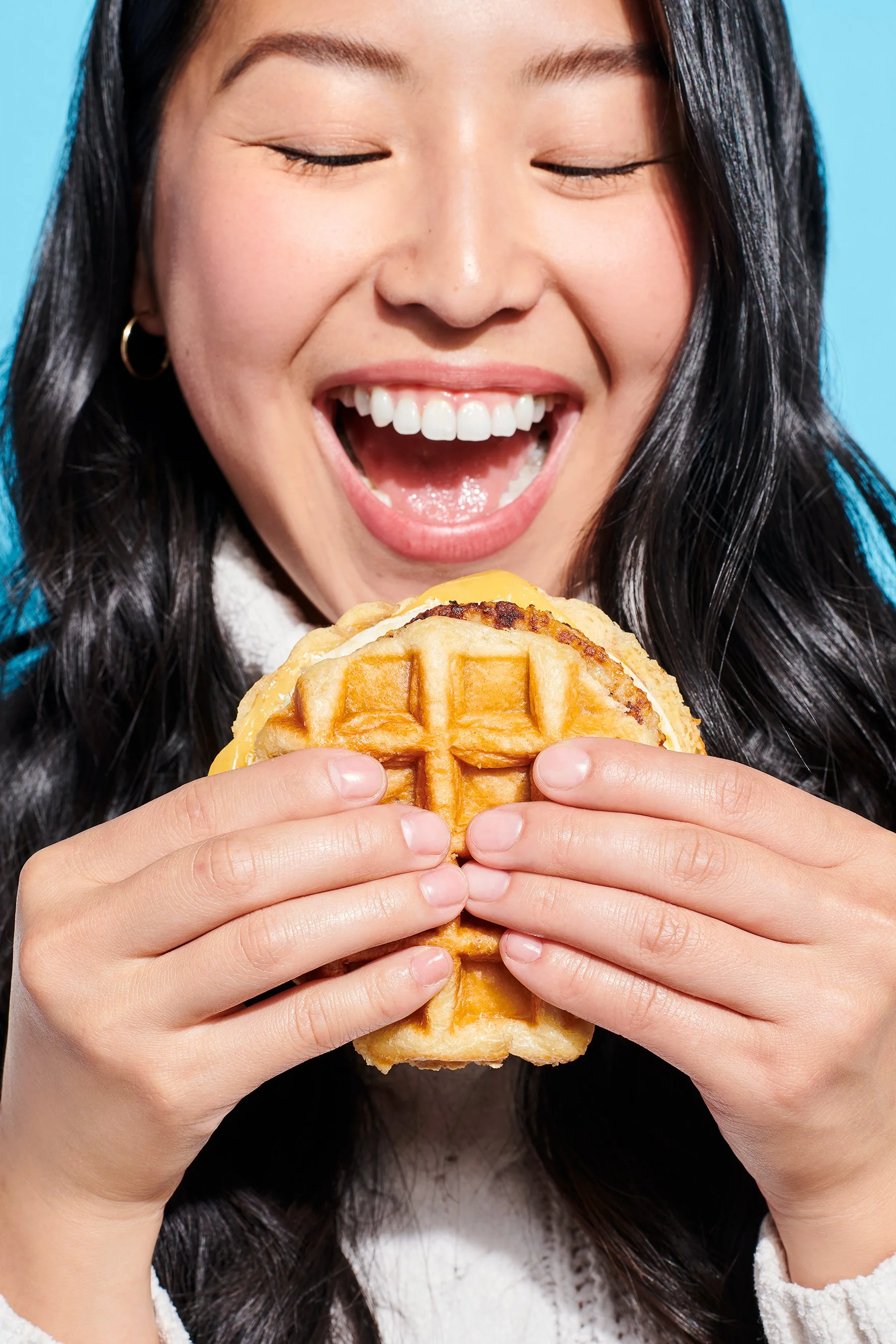 macro image of woman biting a waffle breakfast sandwich