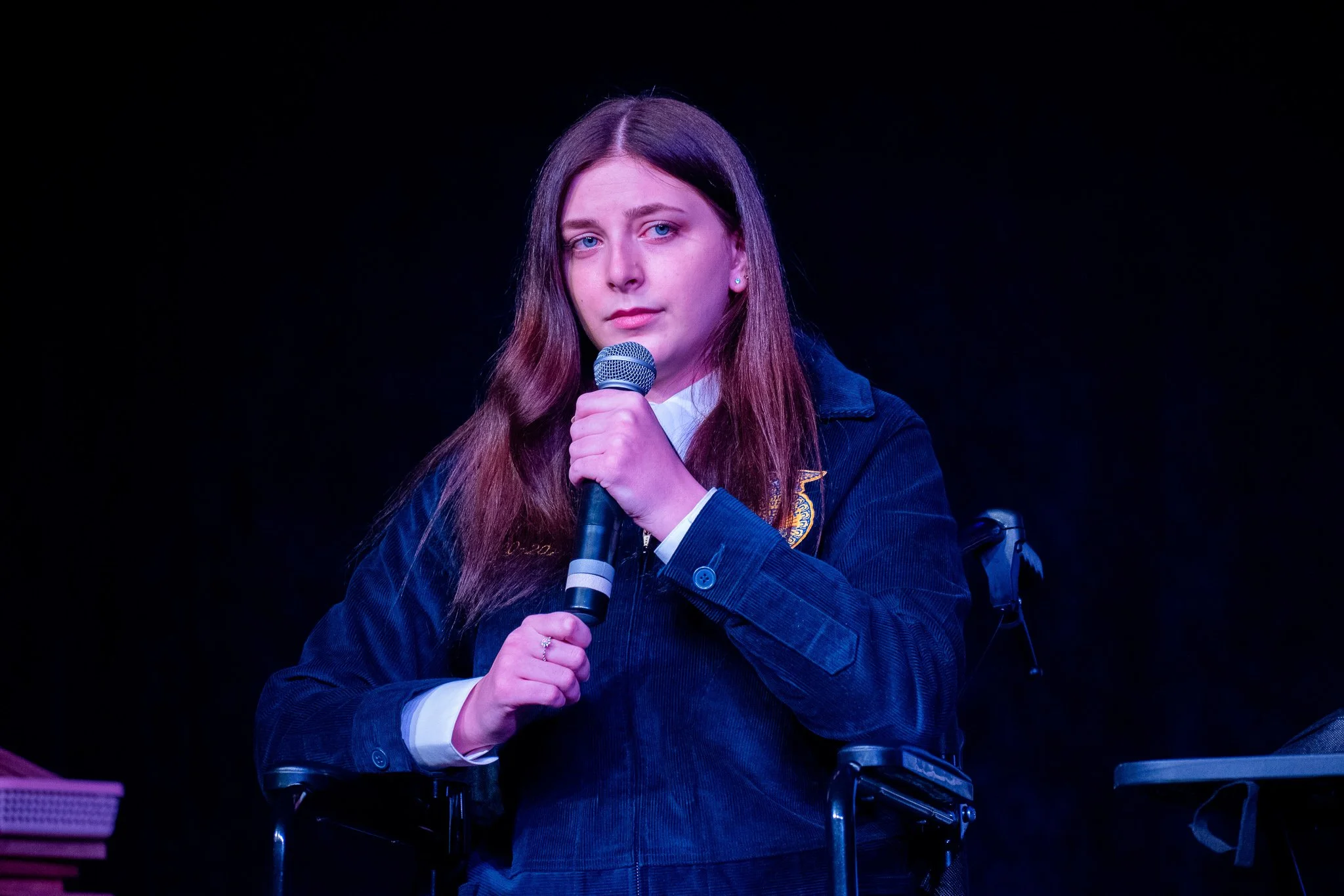 A young woman with long brown hair holding a microphone during a speech or performance.