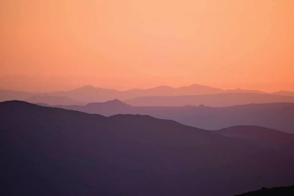 A landscape of mountains during sunset or sunrise with shades of pink and purple in the sky.