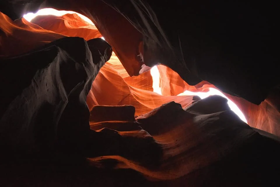 Inside a narrow slot canyon with smooth, flowing sandstone walls illuminated by sunlight streaming from above.