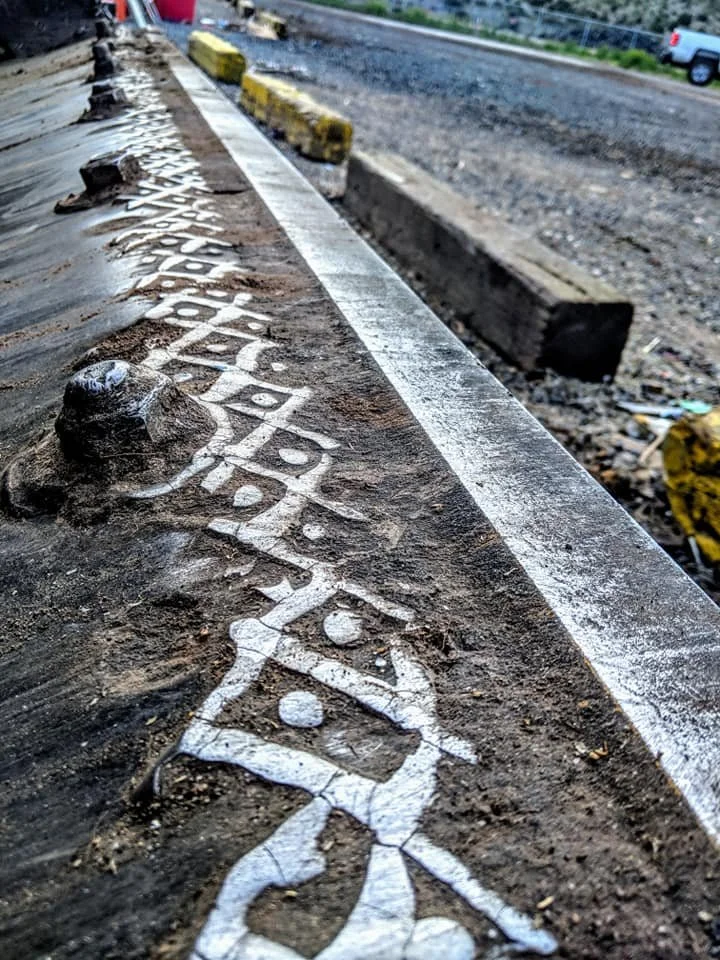 Close-up of a loader bucket with beautiful welded markings and patterns, with a construction site and a road in the background.