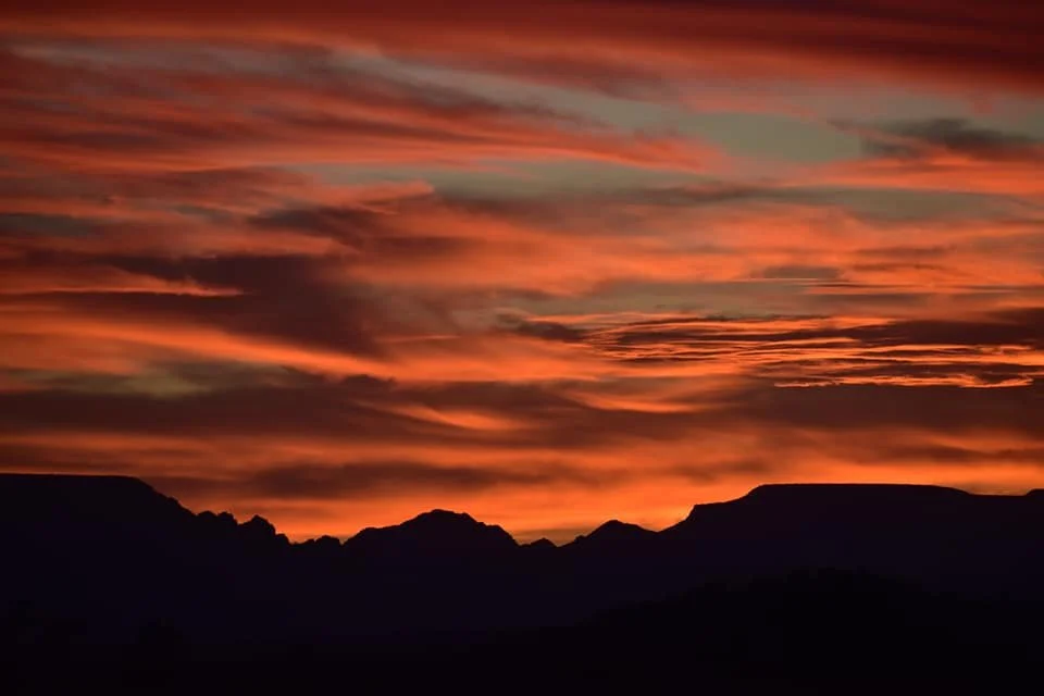 A vibrant sunset over a silhouette of mountains with orange, pink, and purple clouds in the sky.