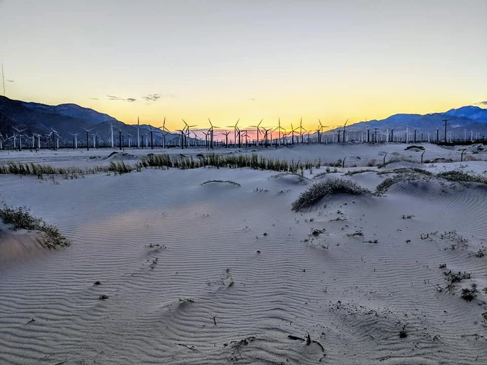 Sand dunes with wind turbines in the distance at sunset, mountains in the background