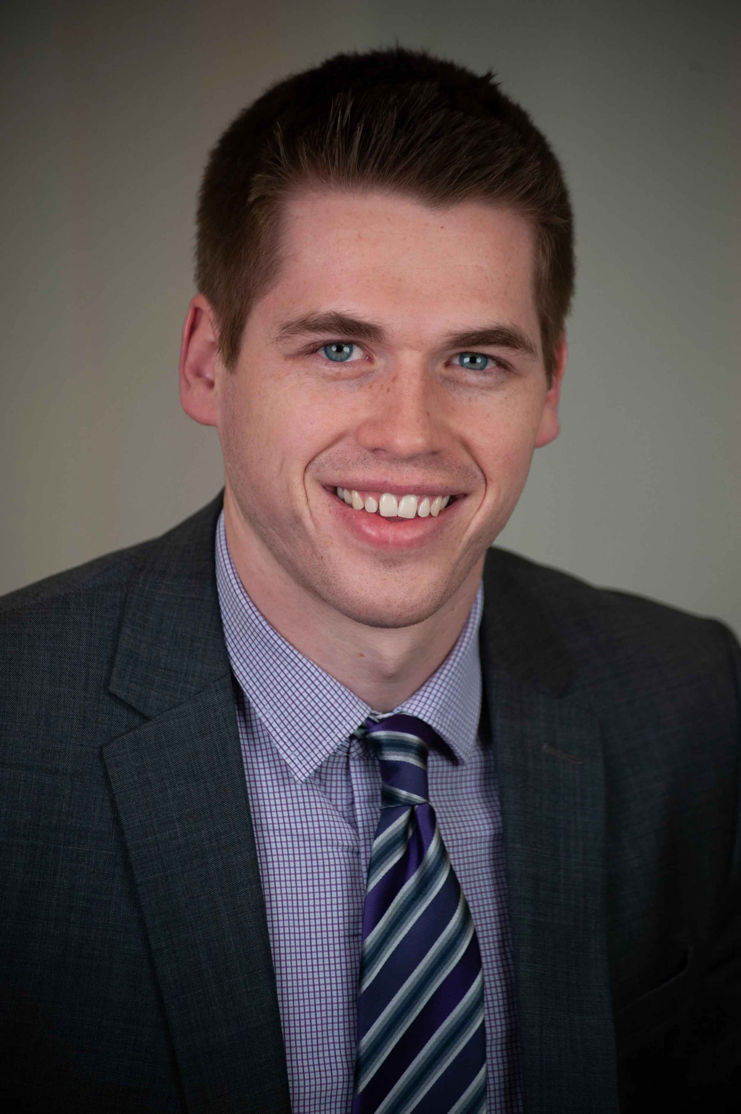 Professional headshot of Dr. Jameson with blue eyes and brown hair, wearing a dark suit, and striped tie, smiling against a gray background.