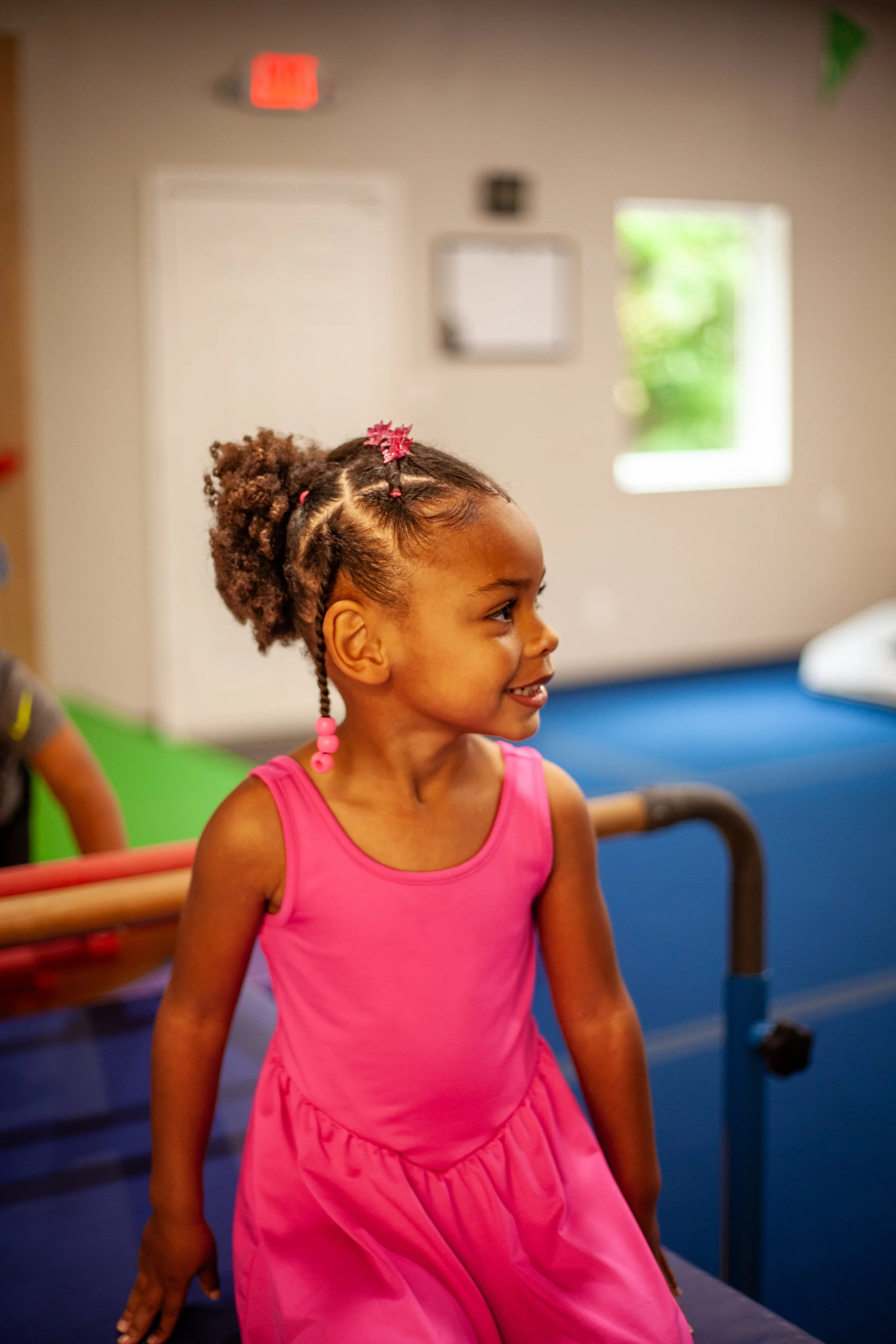 Two young children playing on a gymnastic bar indoors, smiling and having fun.