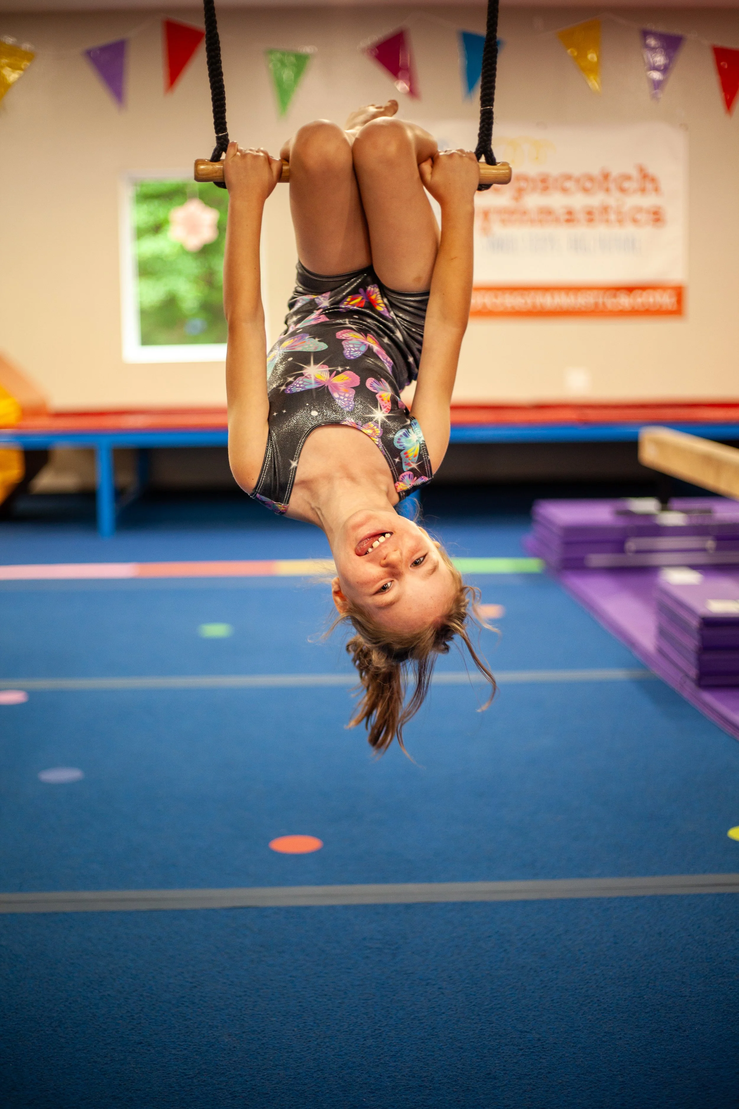 Children practicing gymnastics bridge pose on blue mat in a gym setting.