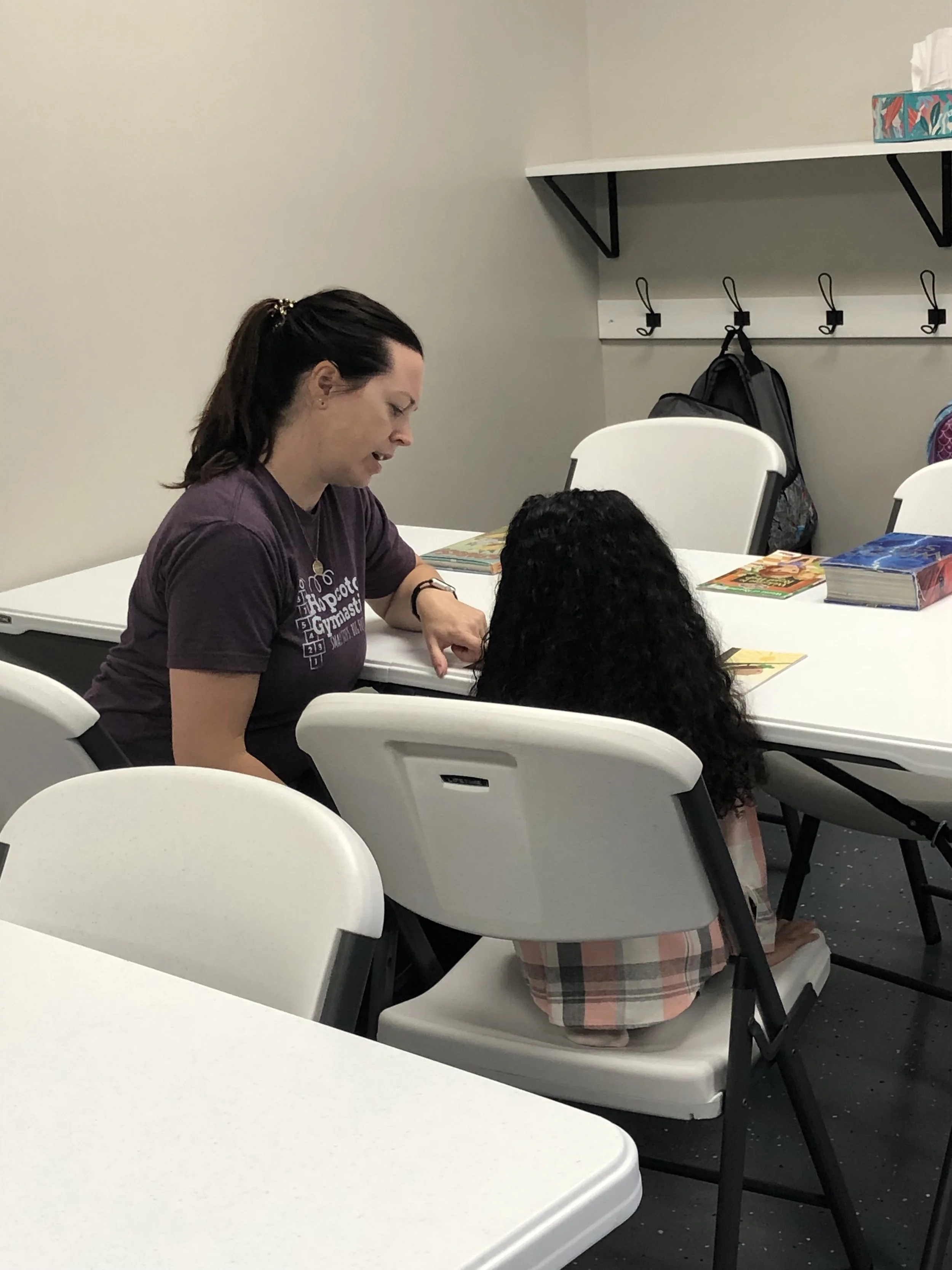 Teacher and child sitting at a table with books in a classroom setting.