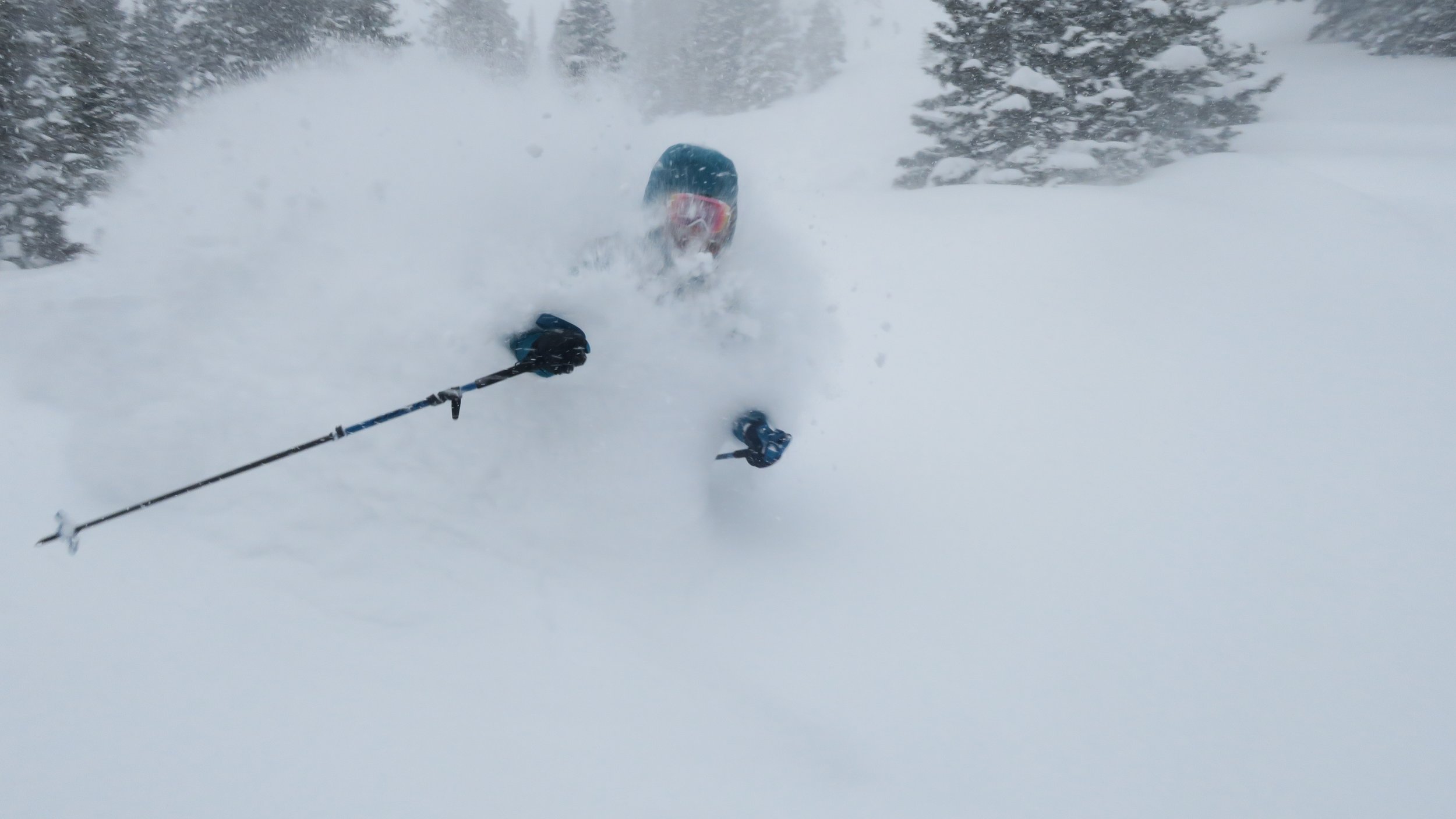 A skier wearing a helmet and goggles skiing through deep snow in a snowy landscape, surrounded by snow-covered trees.