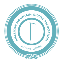 Circular logo of the American Mountain Guides Association featuring a stylized mountain peak and a vertical line, with the text surrounding it.