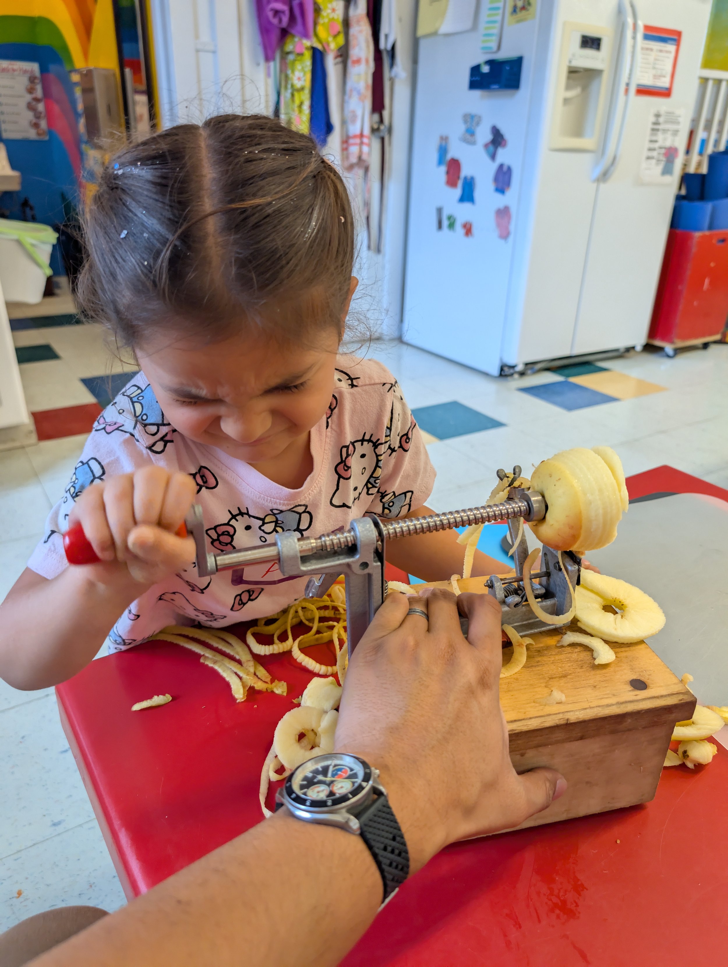 A girl struggles to peel an apple with a manual peeler and corer.