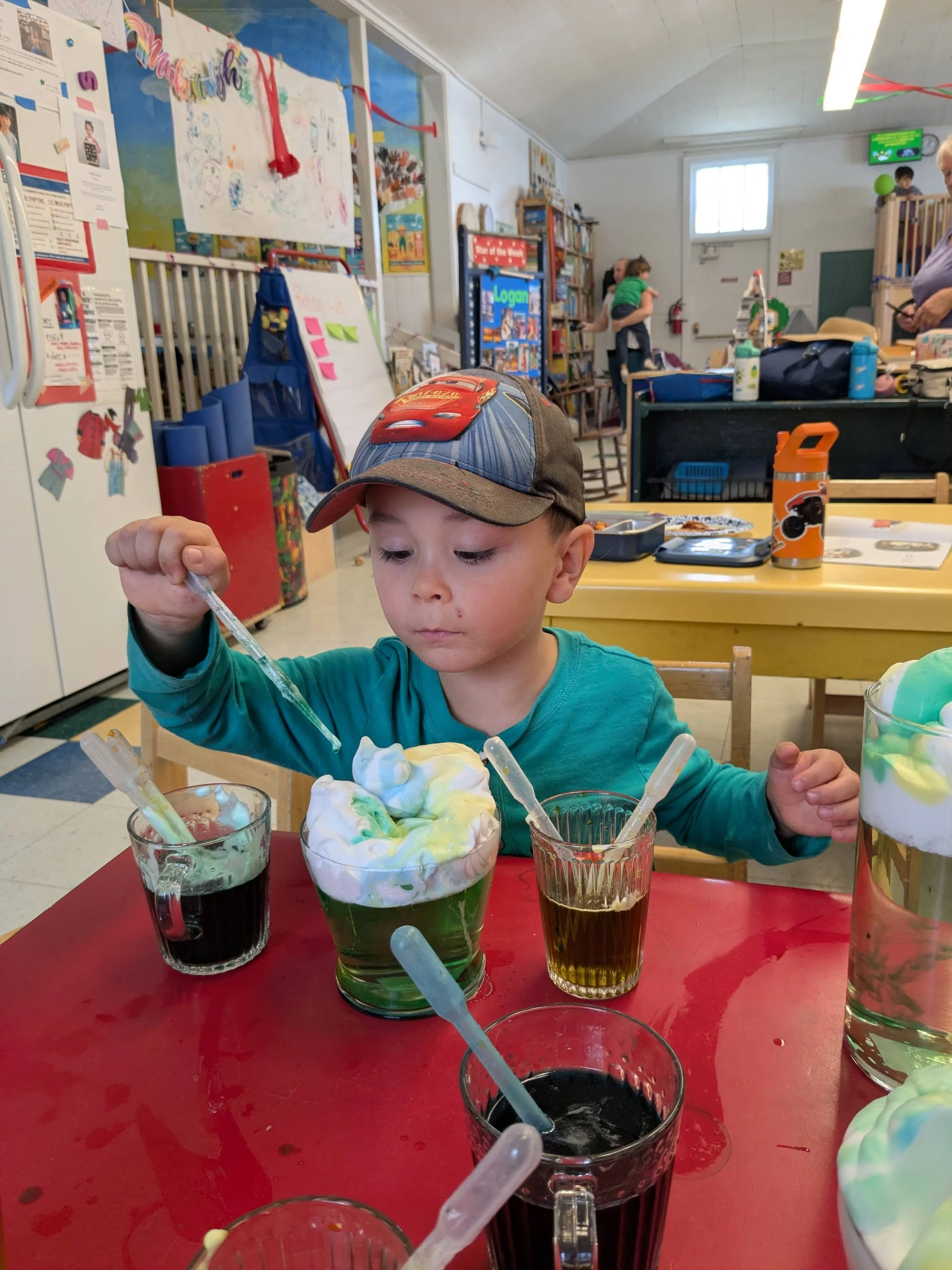 A boy uses a pipette dropper to mix colorful solutions, making 'rain' with shaving cream.