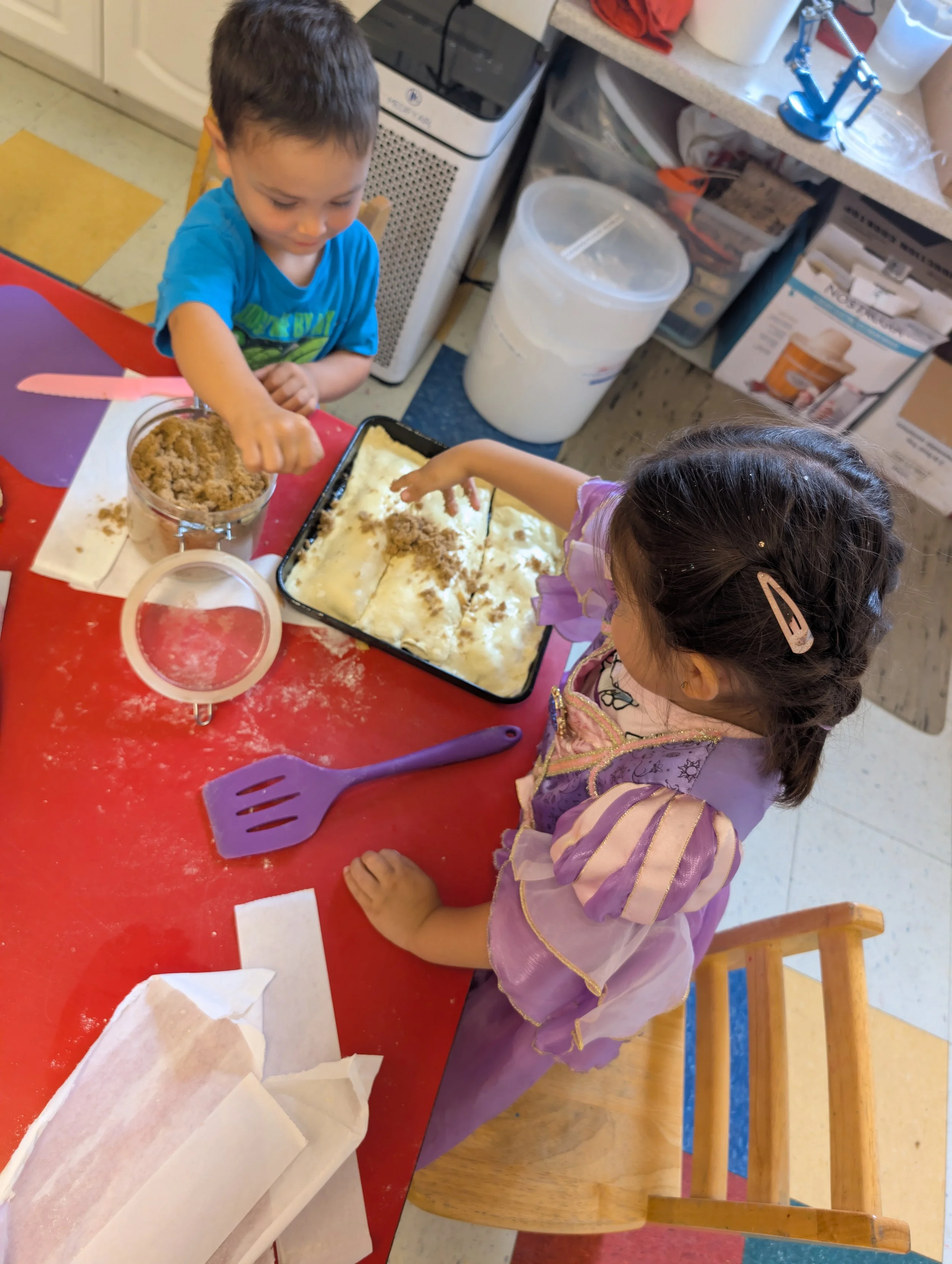 Two kids making a pastry and sprinkling brown sugar with their hands overtop.