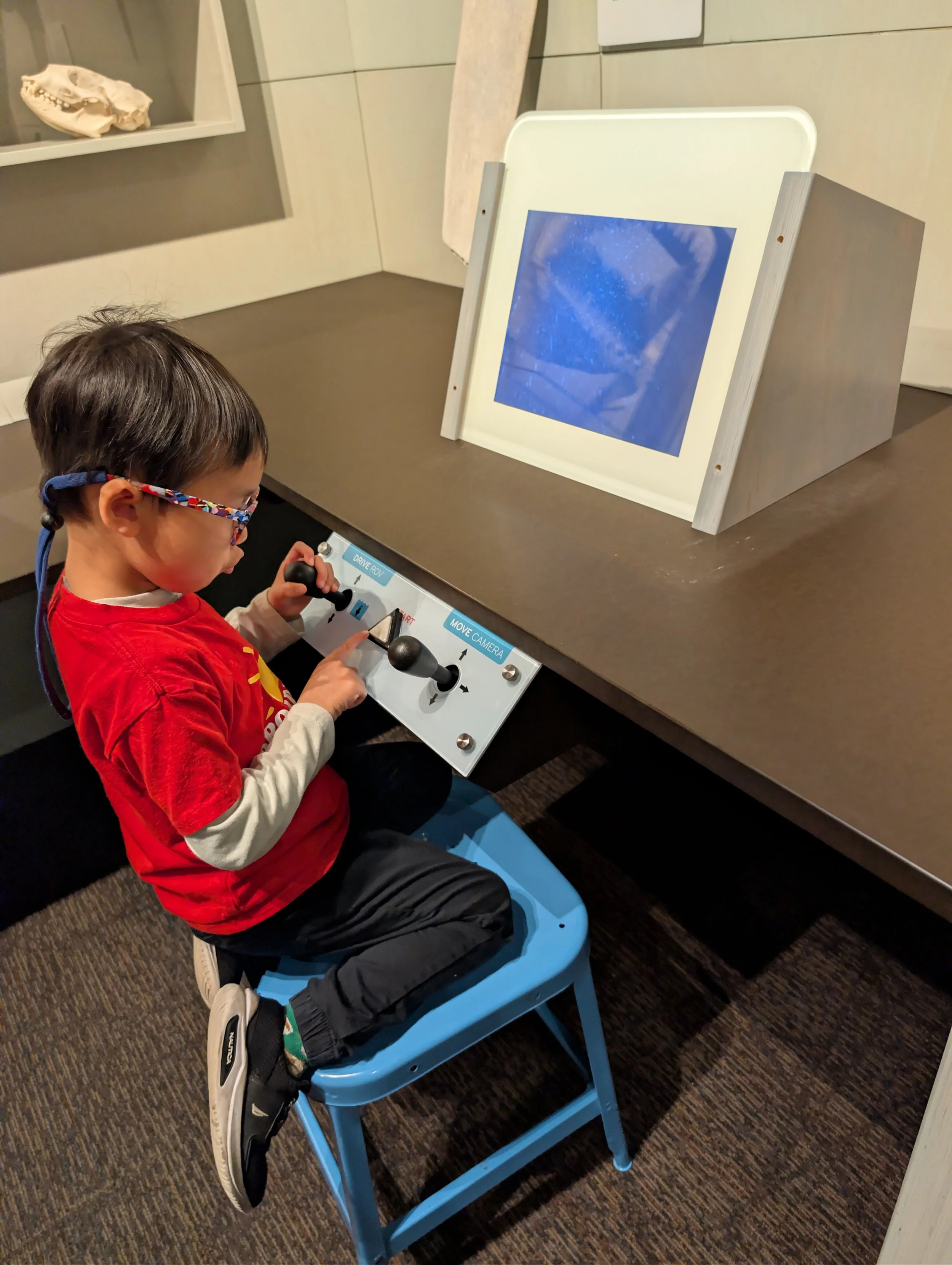 A child uses two toggle joysticks to navigate another exhibit at the OCMA, one moves the RCV, the other moves the Camera.