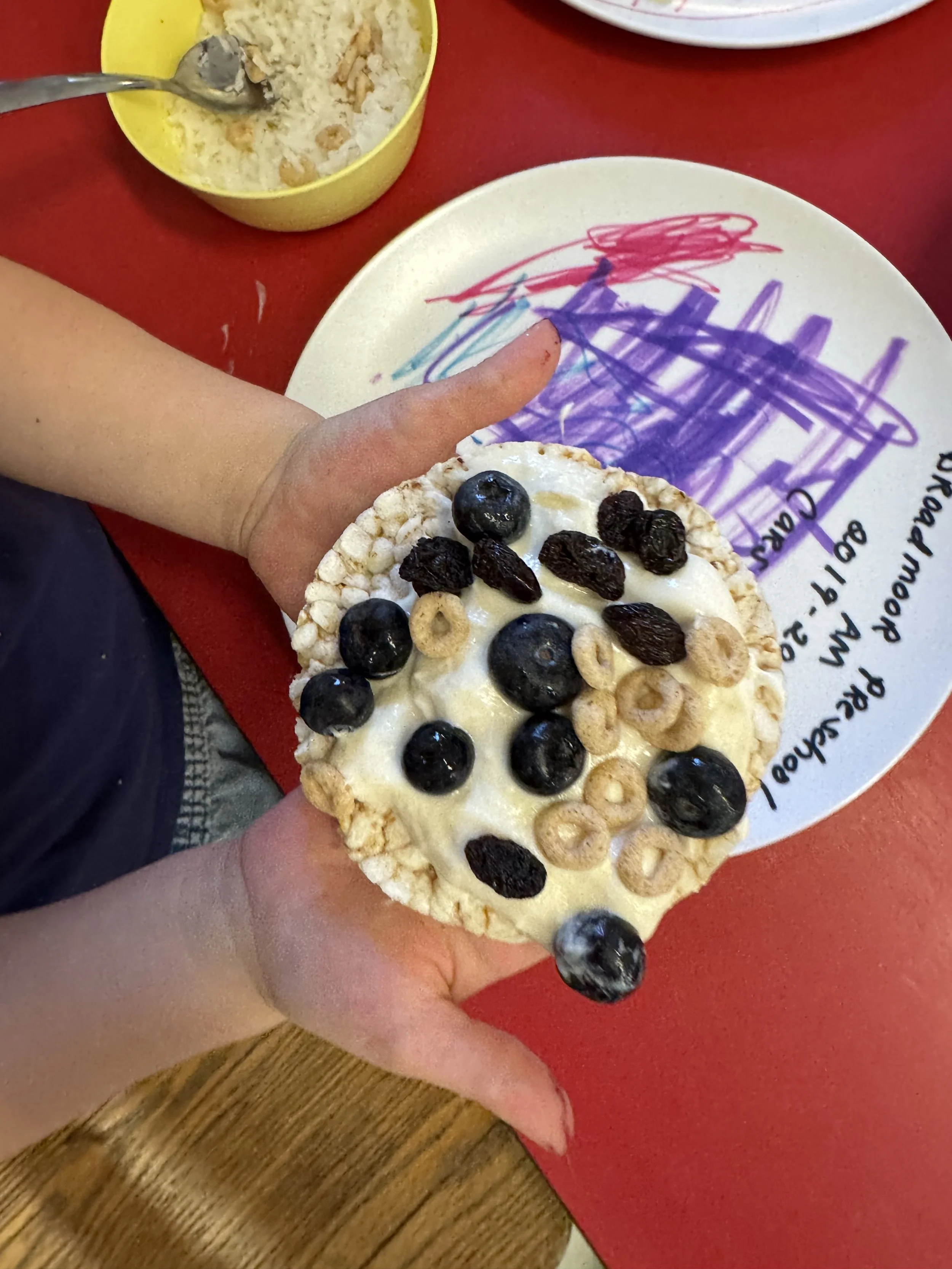 Little hands hold a rice cake decorated with blueberries and cheerios
