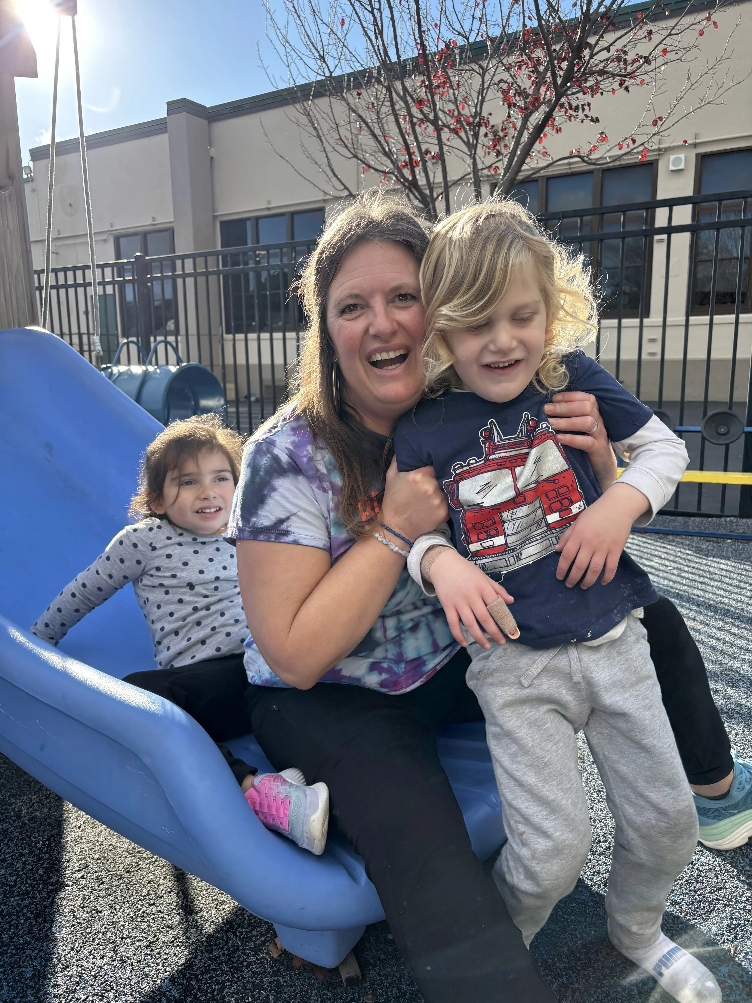 A teacher at the bottom of a slide with two kids.