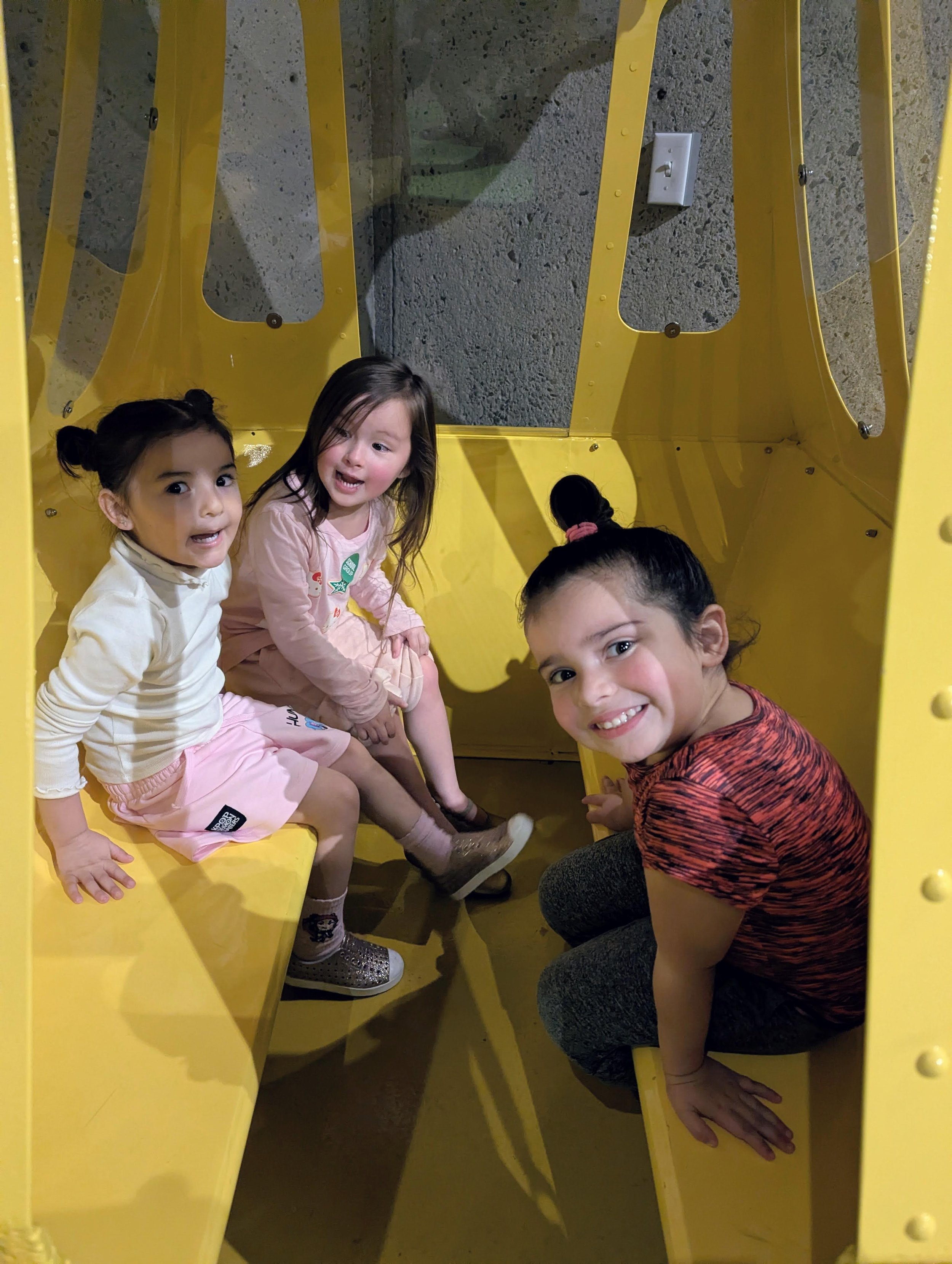 Three children sit in a metal structure (may be a metro train or tram car).
