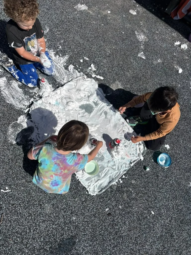 Three Children play with a giant tray filled with shaving cream.