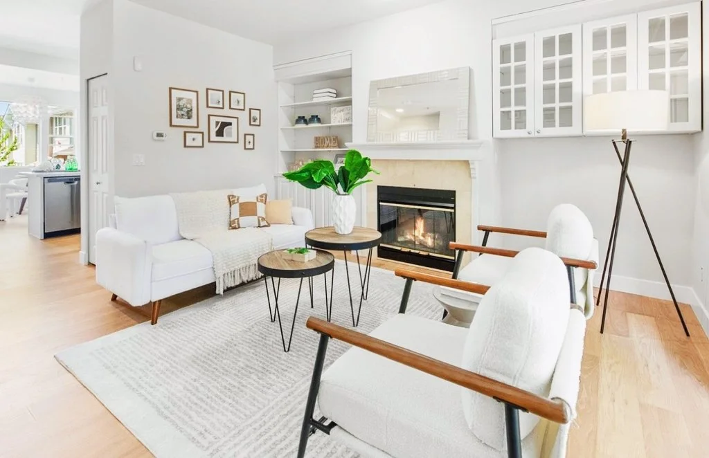 Living room with white sofa, two white armchairs with wooden arms, a fireplace, a large potted plant, and wall art.