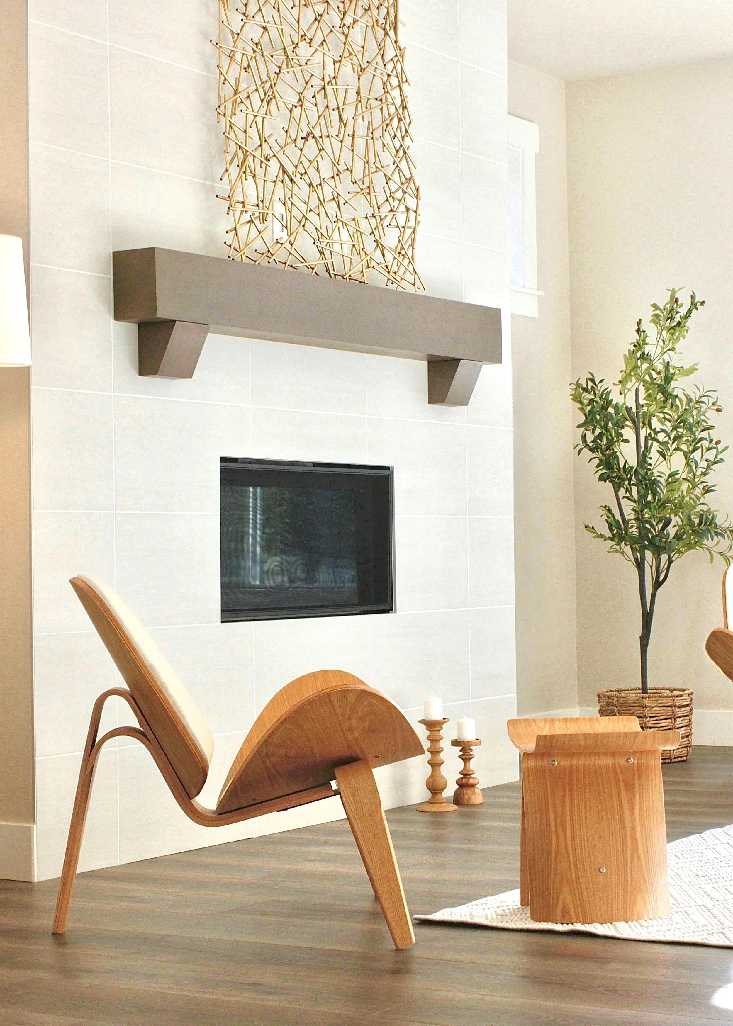 Modern living room with a wooden lounge chair, a small wooden side table, a fireplace, and a tall potted plant.