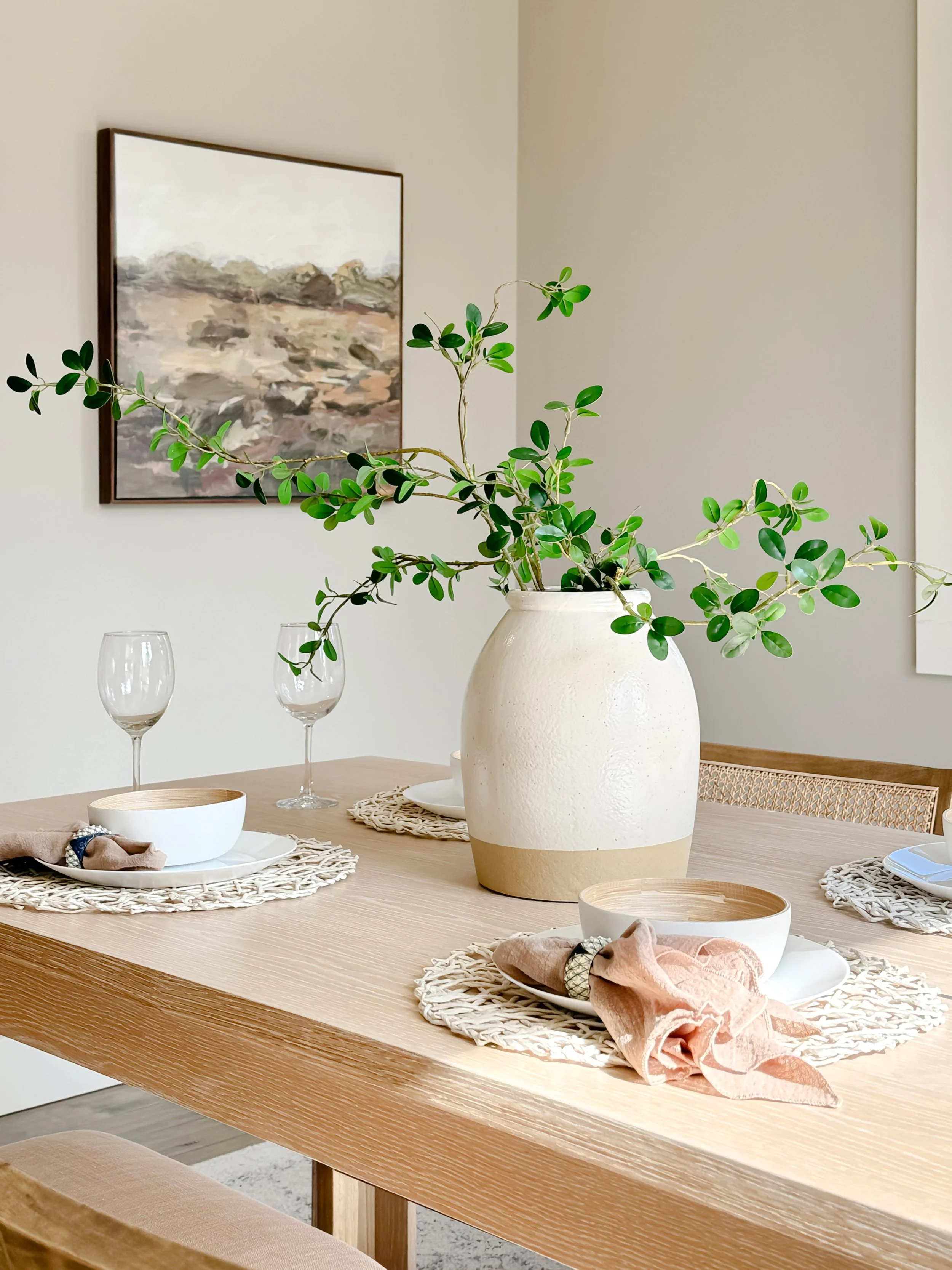 Decorative wall art made from black metal honeycomb frames with woven wooden elements, flanked by two table lamps with wicker bases and white shades on a white console table with baskets and books underneath.