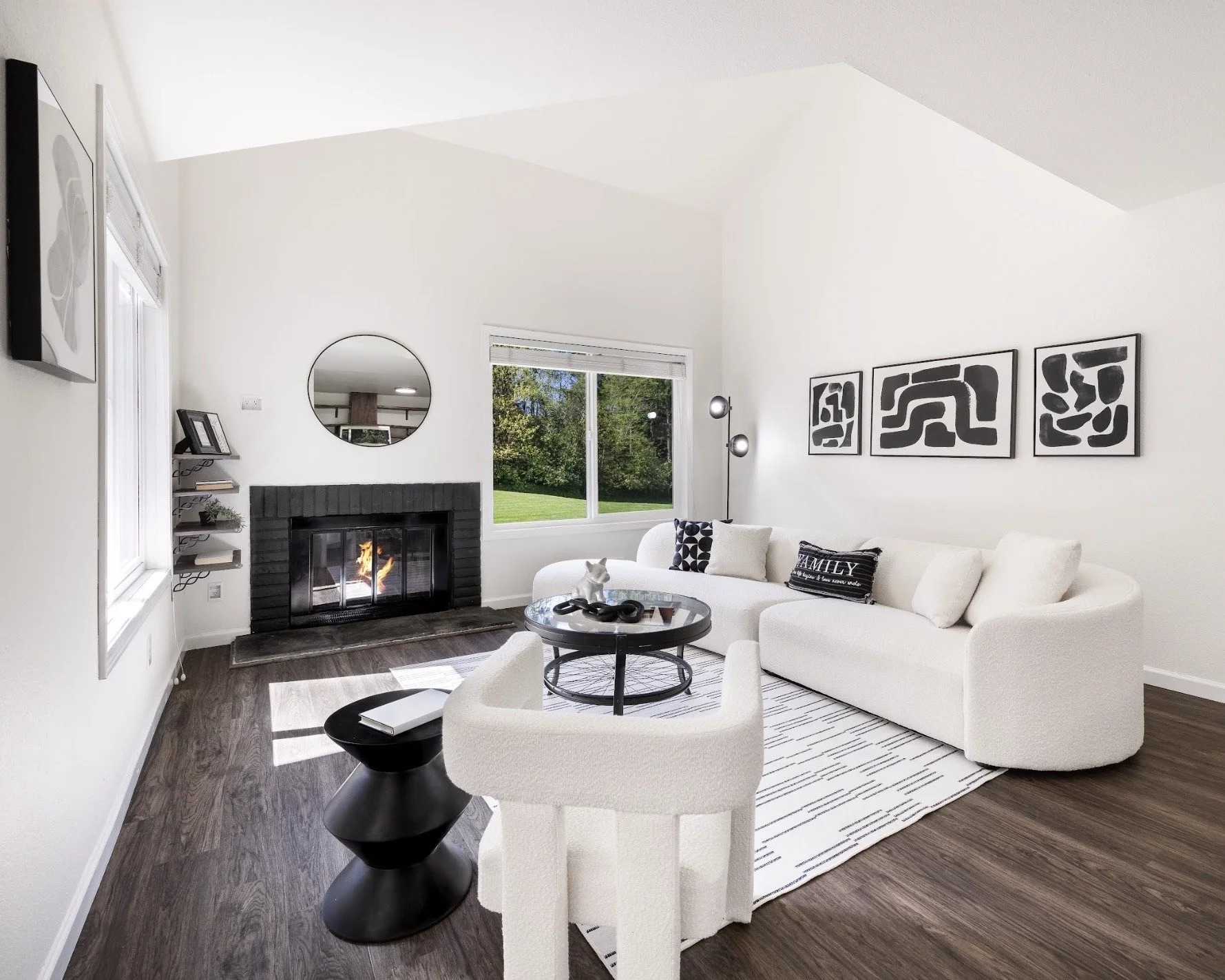 Living room with white sectional sofa, black and white abstract art on wall, and a fireplace with fire.