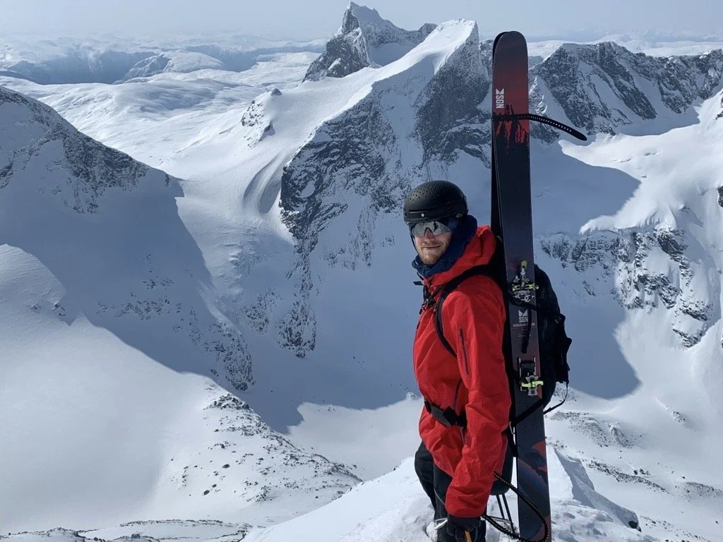 Bård Basberg på eit fjell med ski på sekken og spisse fjell i bakgrunnen.