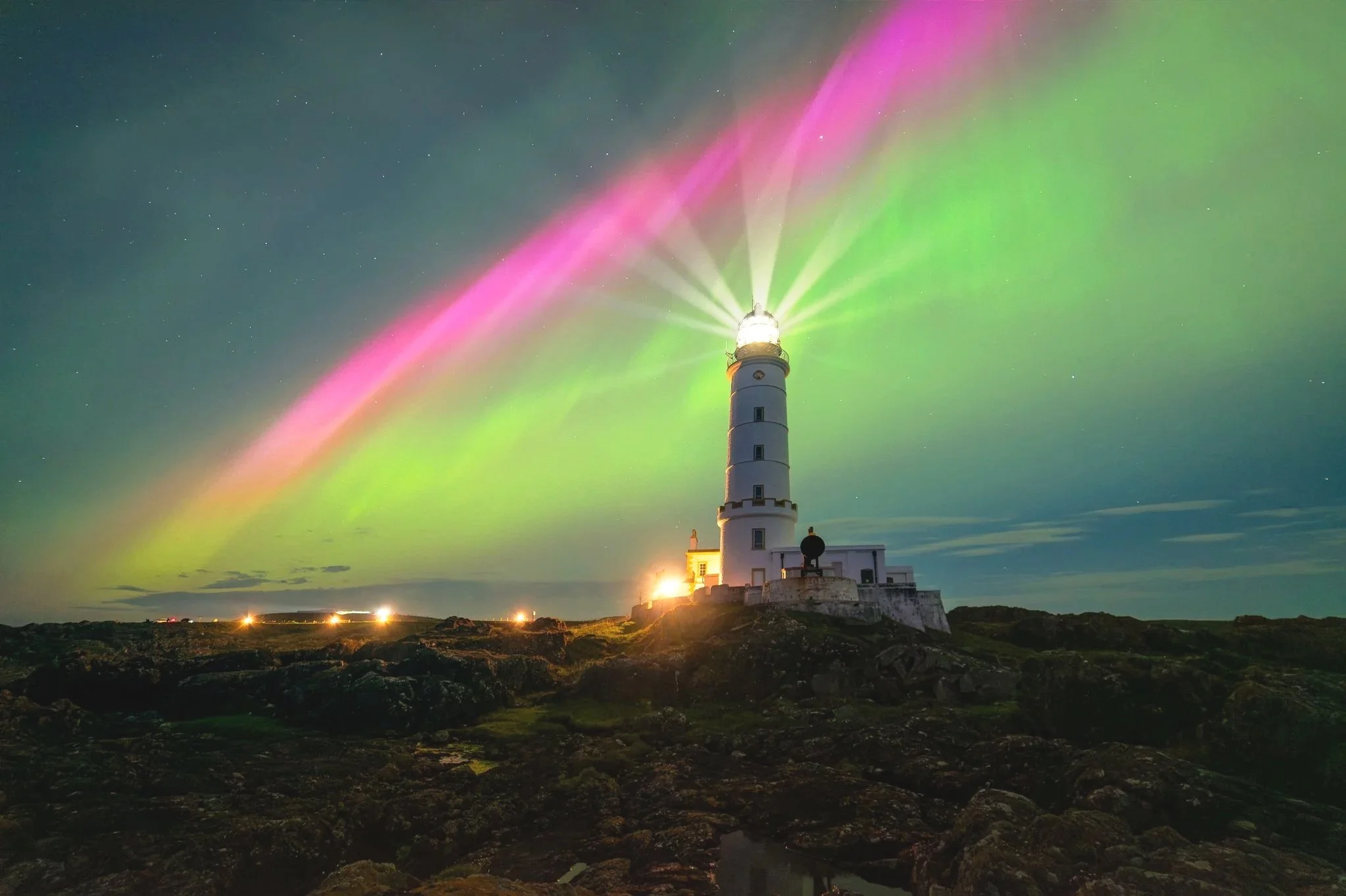 Lighthouse with colorful aurora borealis in the night sky.