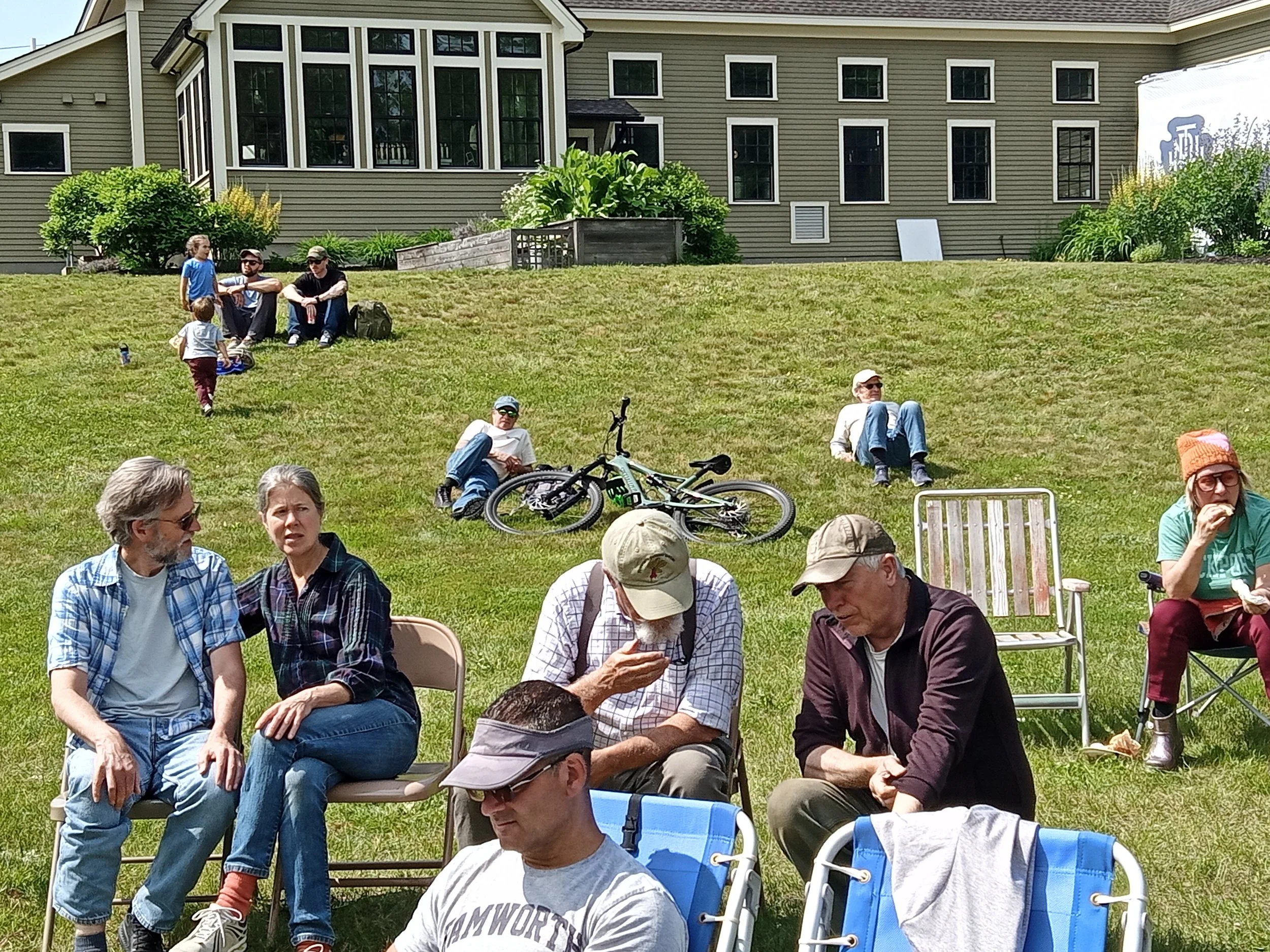 A crowd of people sitting on lawn chair on a grassy hill.