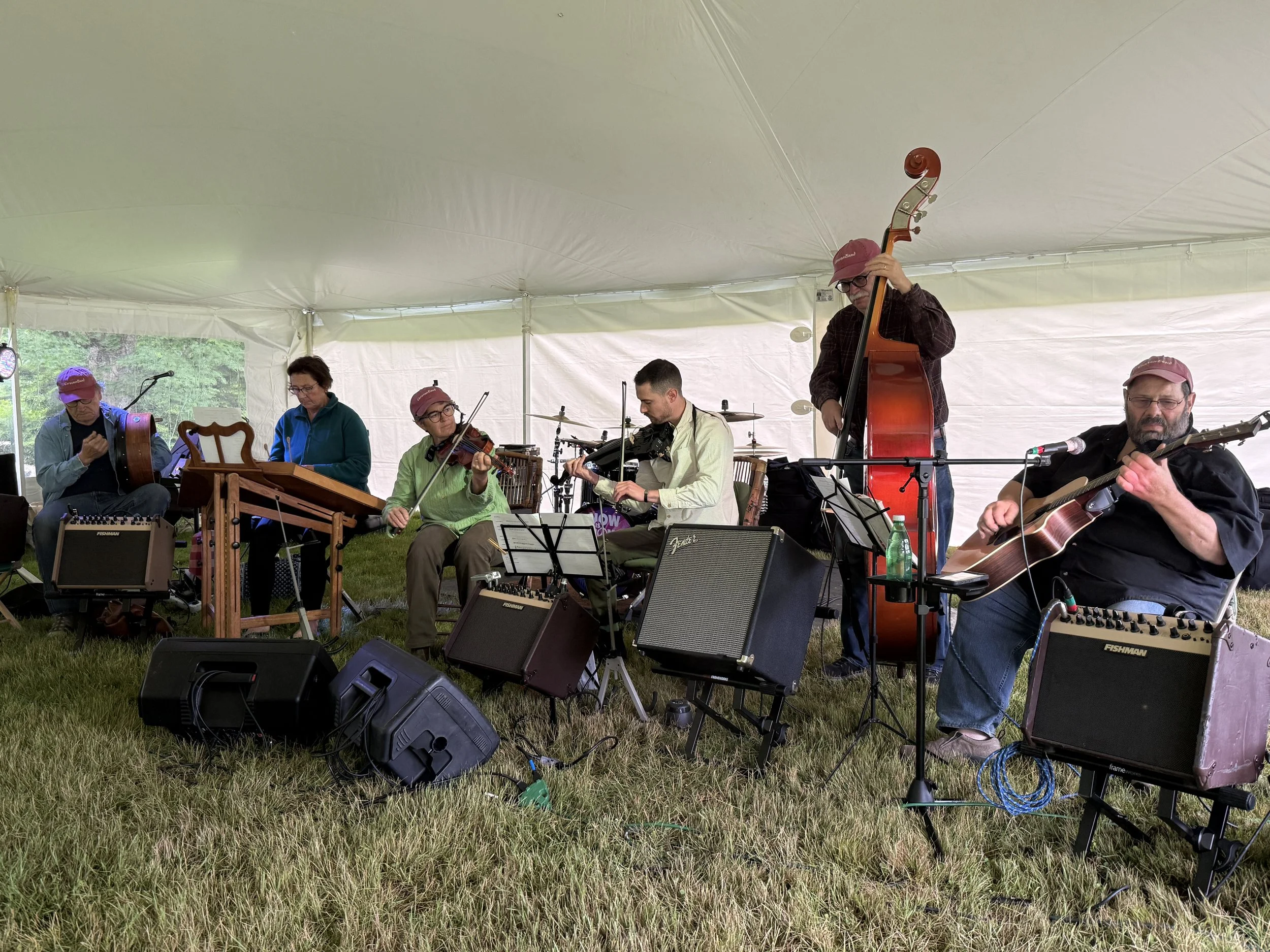 An acoustic band of six musicians performing outdoors under a tent.