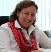 A woman with wavy brown hair, wearing a white blouse and scarf.
