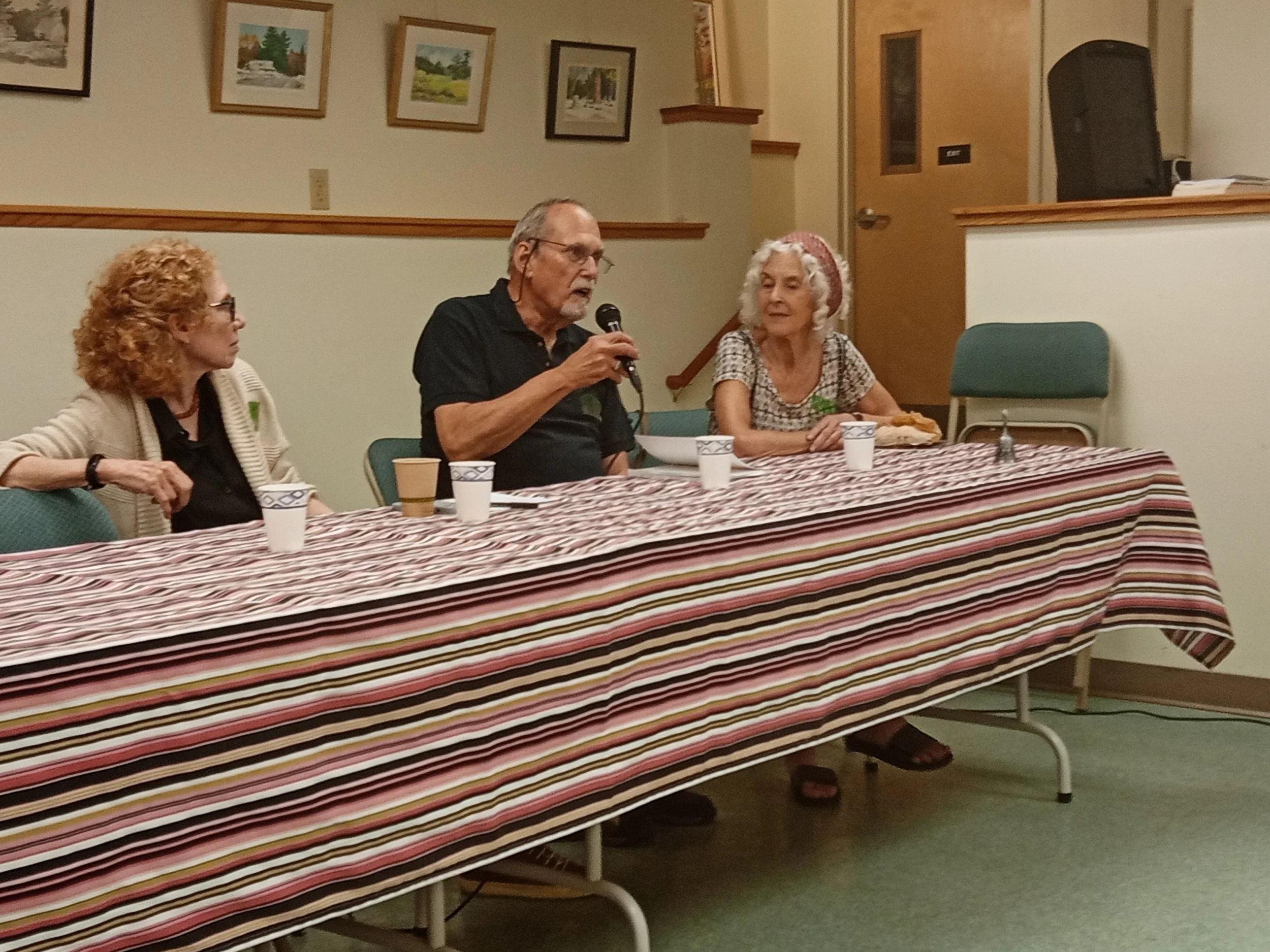 A row of people sitting at a table with a microphone held by the man in the center.
