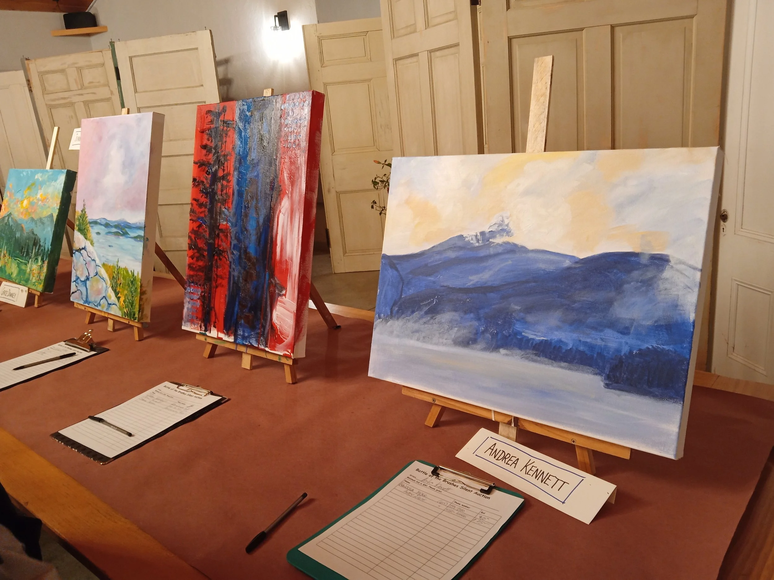 Row of paintings on easels, with clipboard in front of each painting.