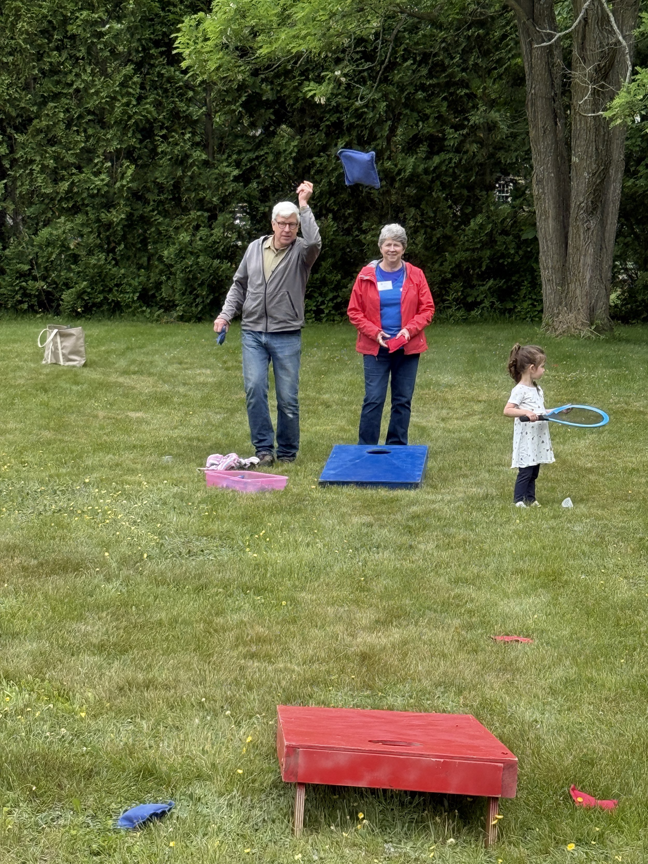 Two people playing beanbag toss while a child plays with a badminton racquet.