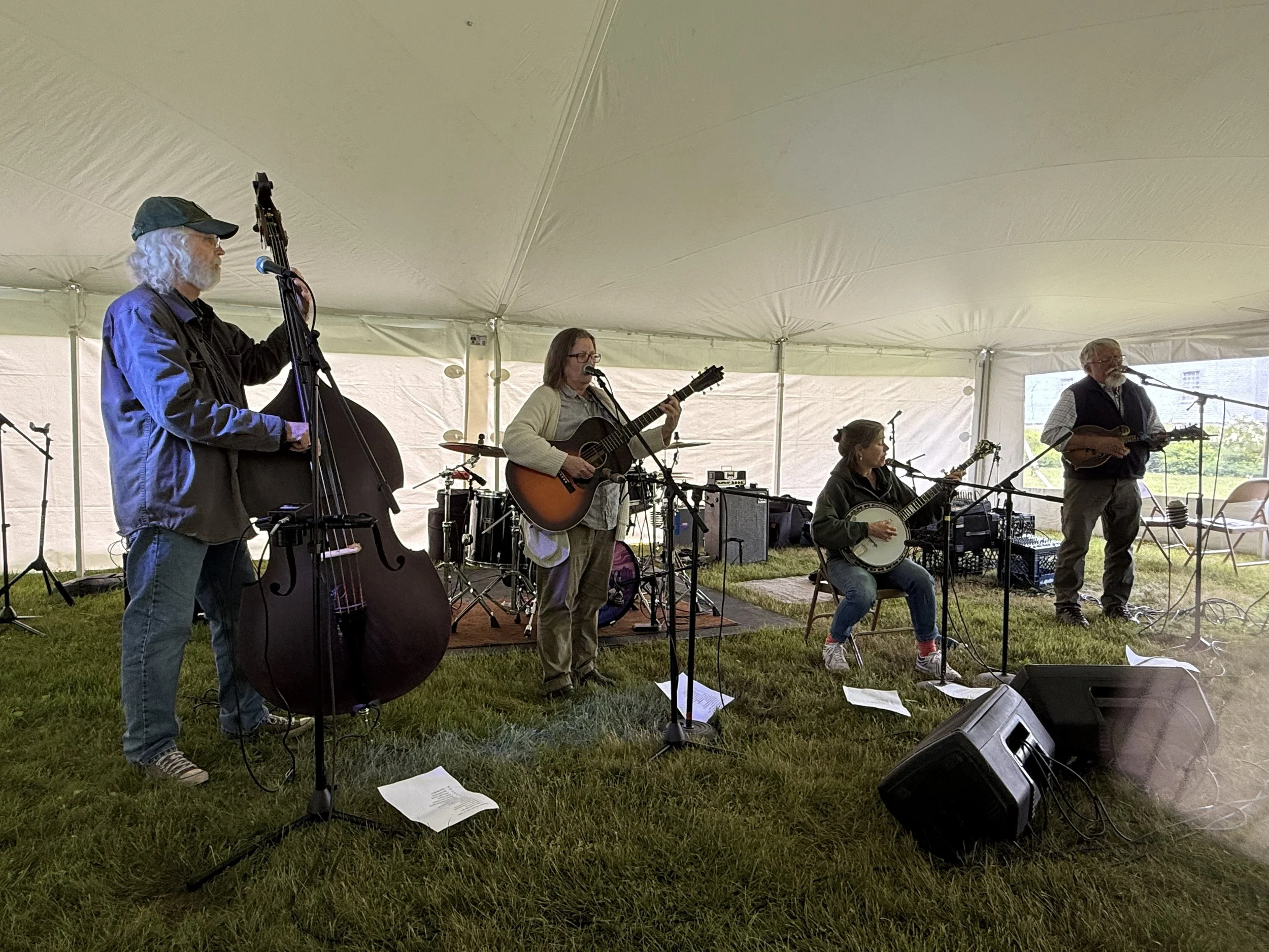 Acoustic folk band playing instruments outdoors under a tent.