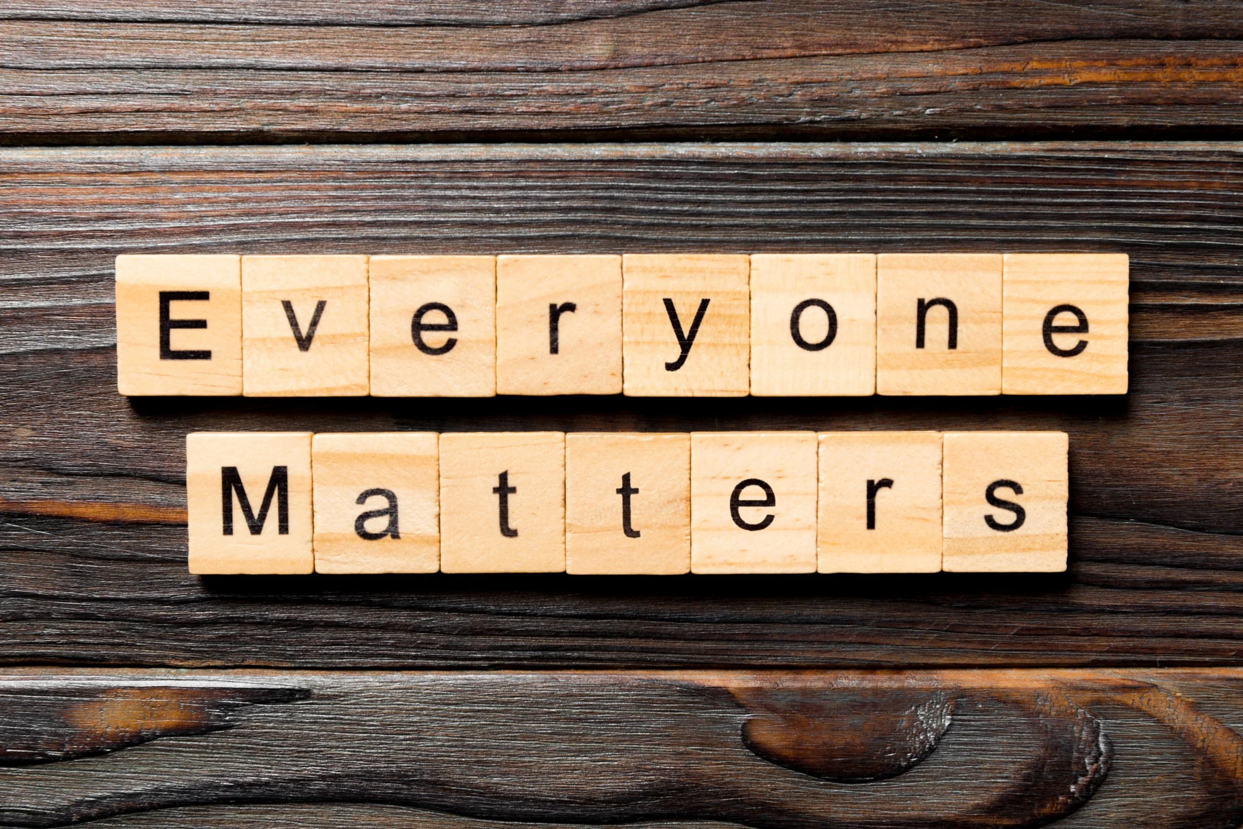 Wooden tiles spelling "Everyone Matters" on a dark wood background.