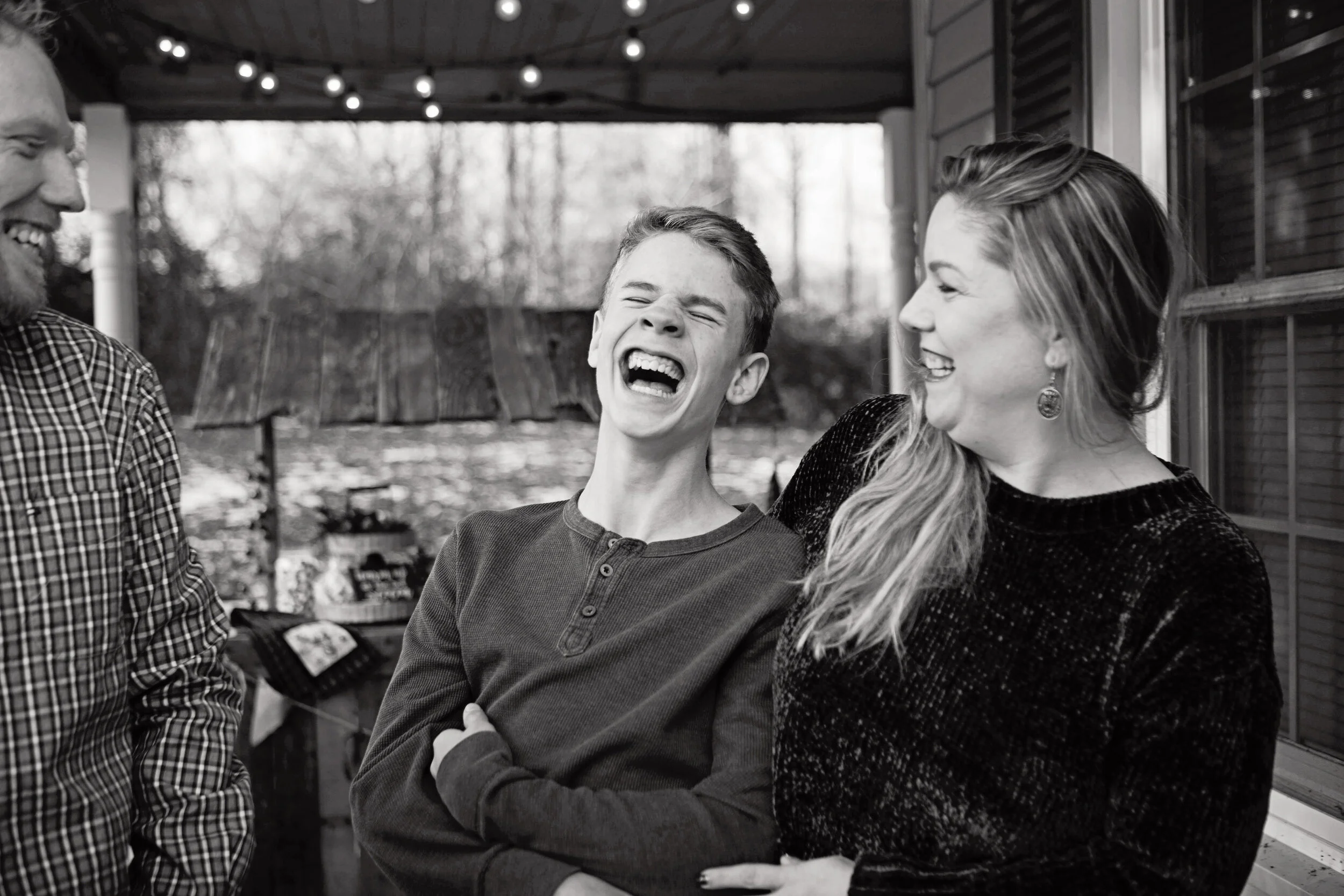 A young man and woman are laughing and smiling, standing close together outside, with a man partially visible on the left side of the image.