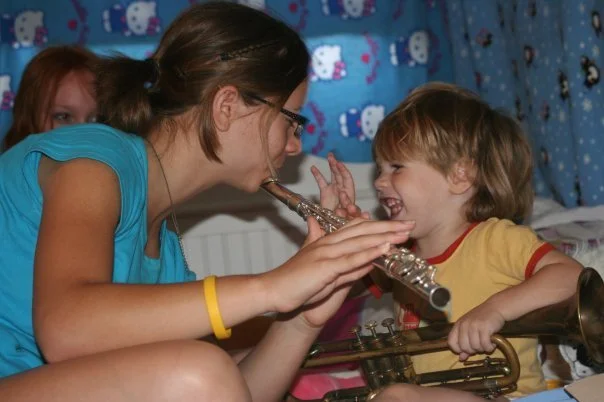 A woman and a young boy playfully pretend to blow a bubble through a trumpet, smiling and having fun.