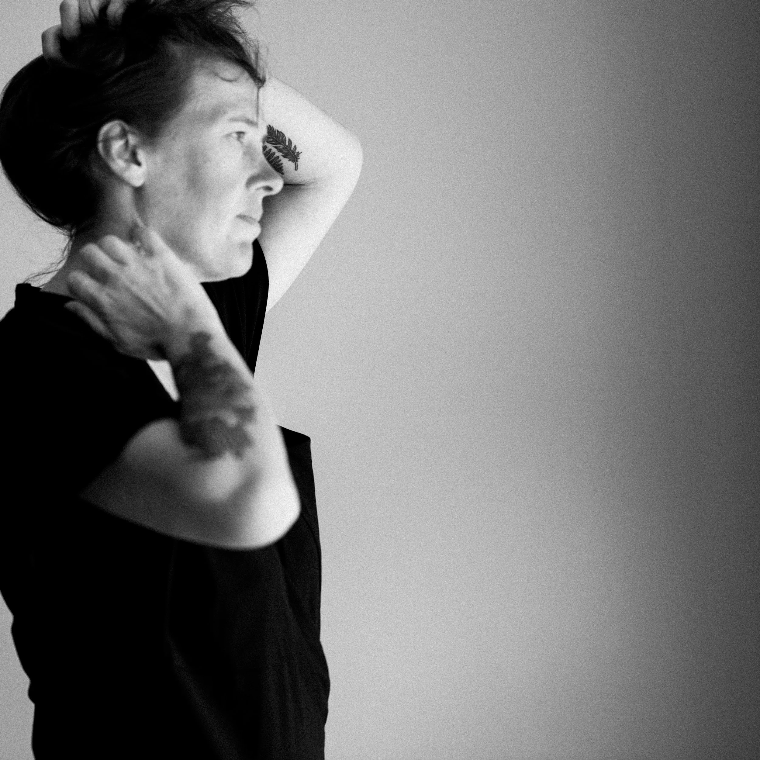 A black and white image of a person with their hands on their head and neck as they gaze at the horizon, showing how embodied support can help you to stay in the present moment.