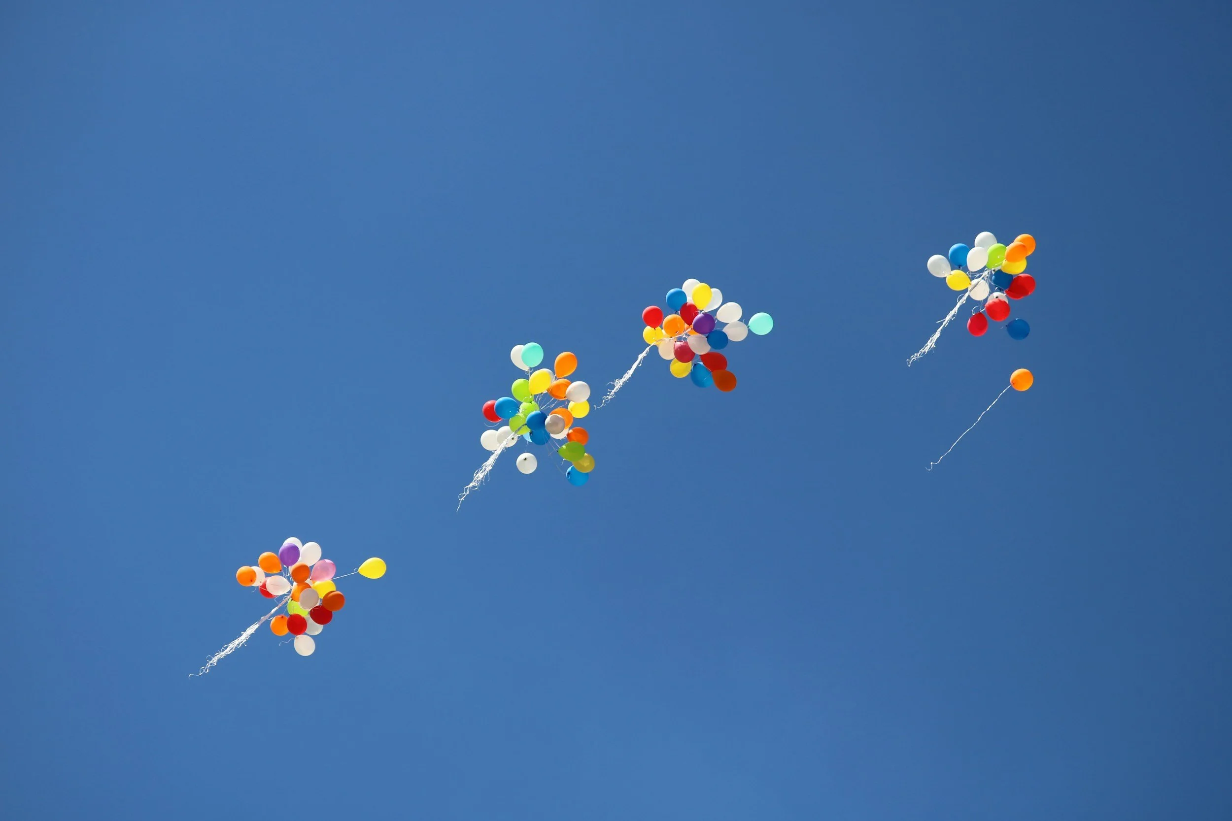 Four bunches of colourful balloons float up into the sky, showing how therapy can help you to let go of what you've been holding onto that's been keeping you stuck.