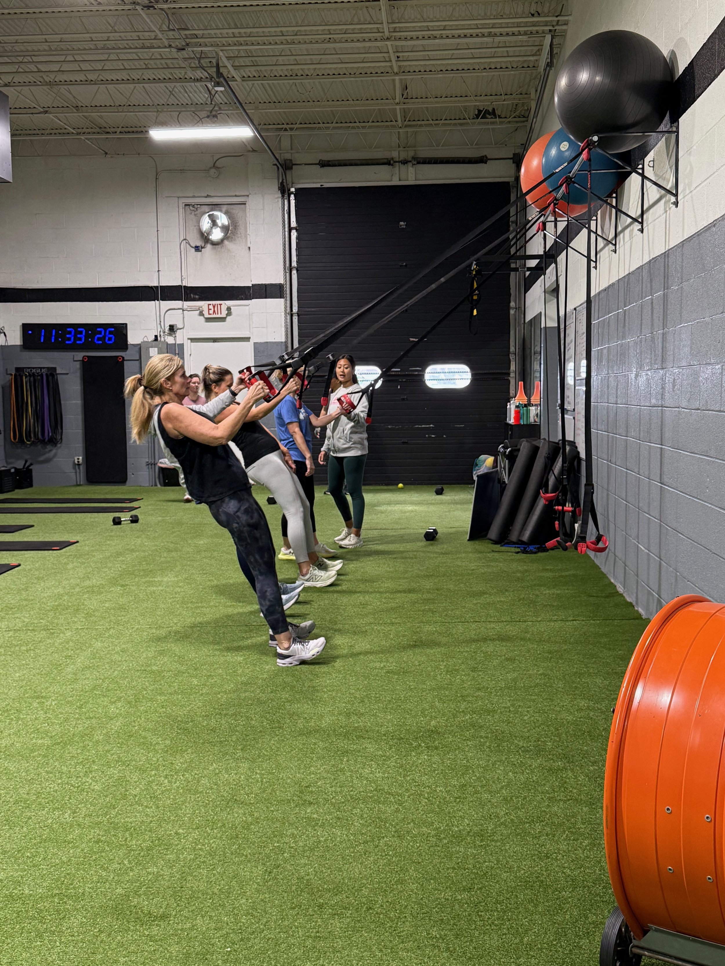 Group of women participating in a fitness class using resistance bands attached to the wall in a gym.