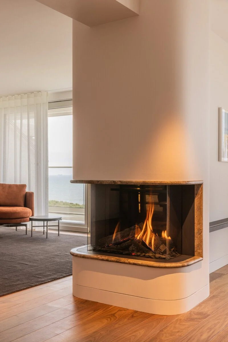 Moderne woonkamer met brandende open haard, fauteuil, salontafel en uitzicht op zee