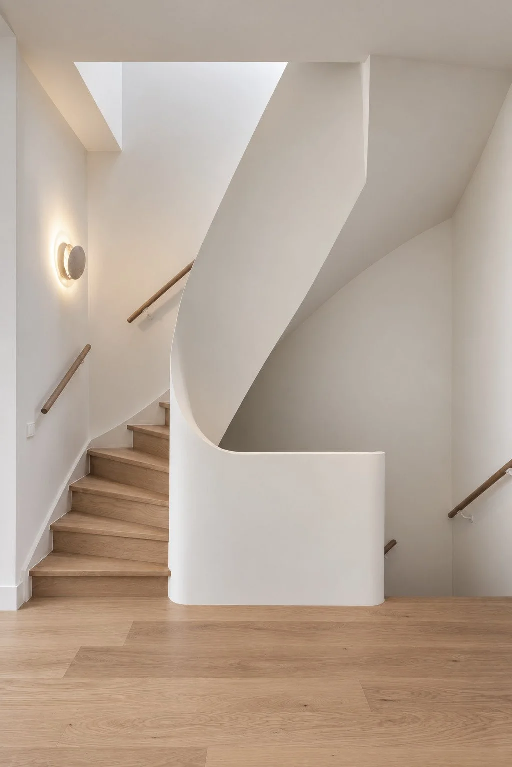 Moderne houten trap met witte, gebogen balustrade, houten leuningen en wandlamp in een minimalistisch interieur.
