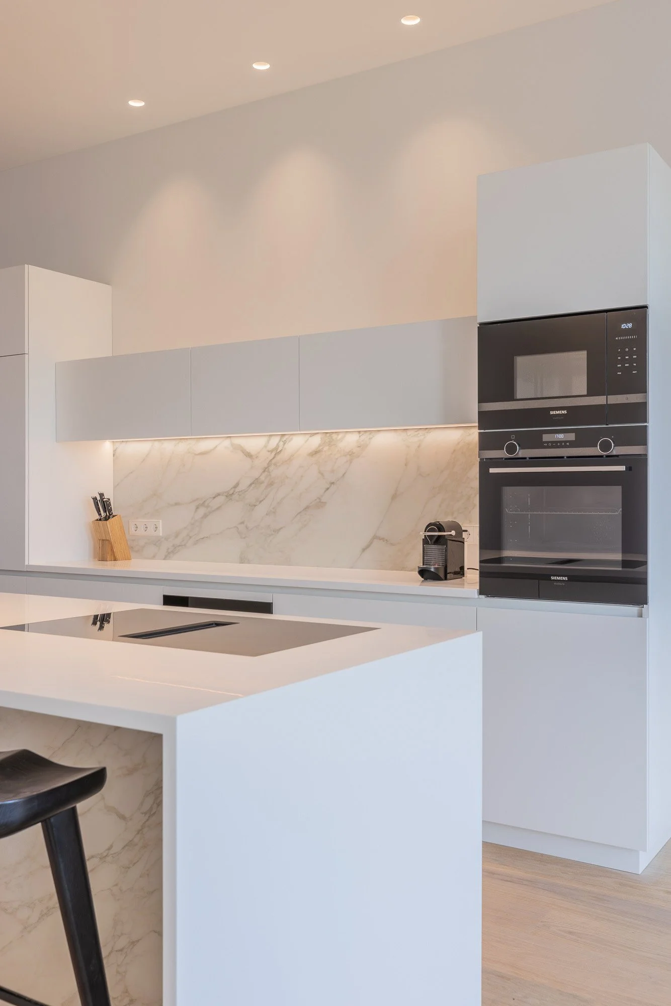 Modern witte keuken met marmeren achterwand, kookeiland, inductiekookplaat, Siemens oven en magnetron