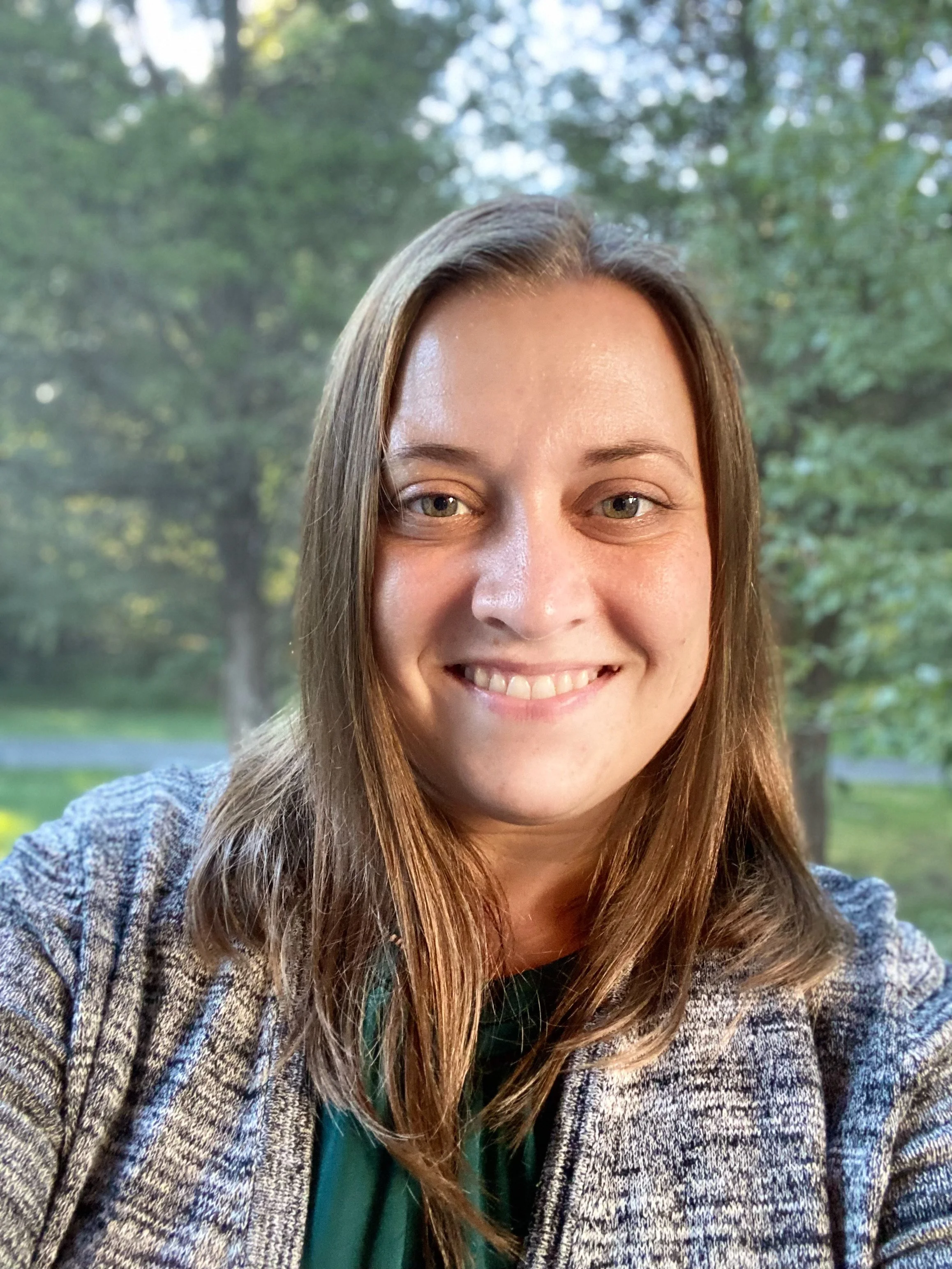 Sthira Sukham Yoga teacher Heidi Eaton standing in front of green trees. She is brown should length hair, big brown eye and a welcoming smile. 