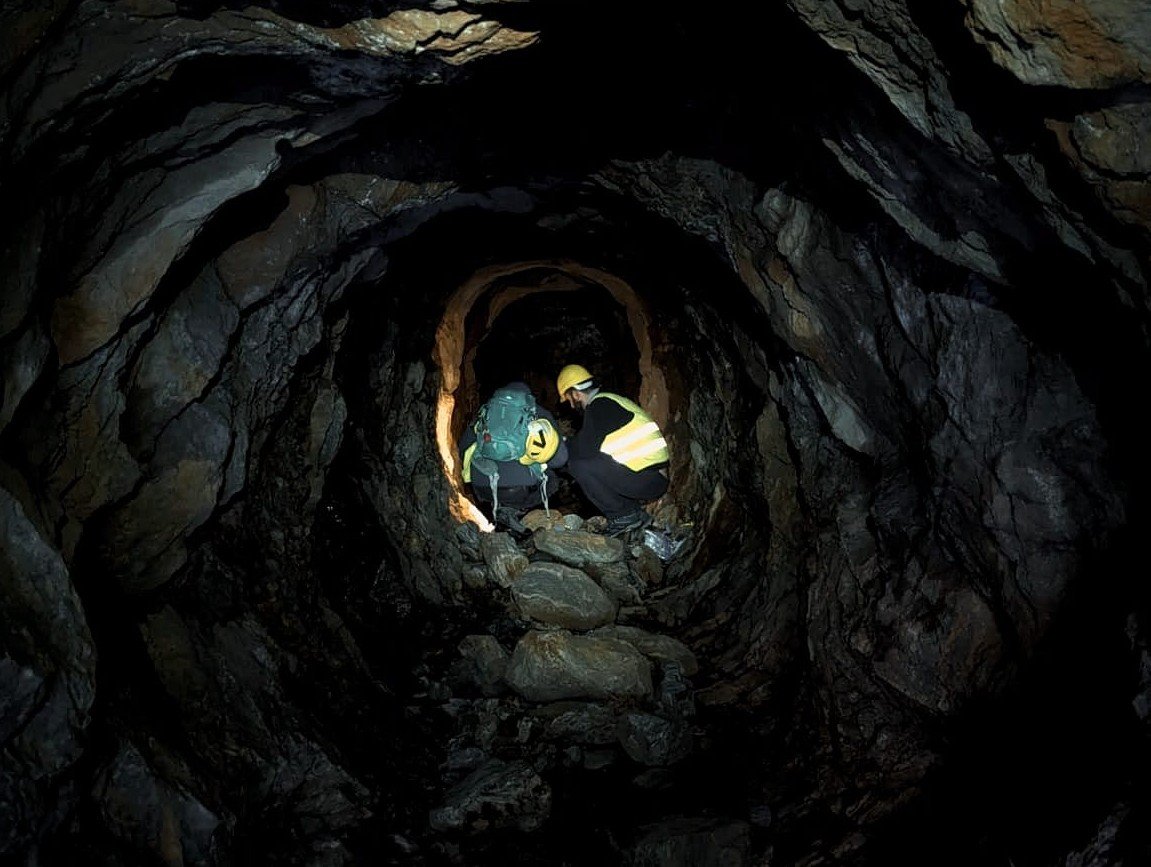 Two people wearing safety equipment within a small mine shaft conducting scientific sampling