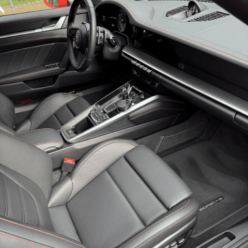 High-end Porsche interior detailing in Cincinnati, showcasing spotless black leather seats with red stitching and a professionally vacuumed driver-side floor.